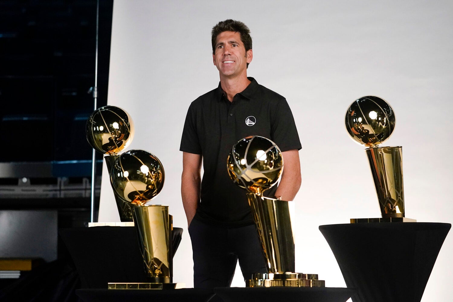 Bob Myers posing with NBA Championship trophies.