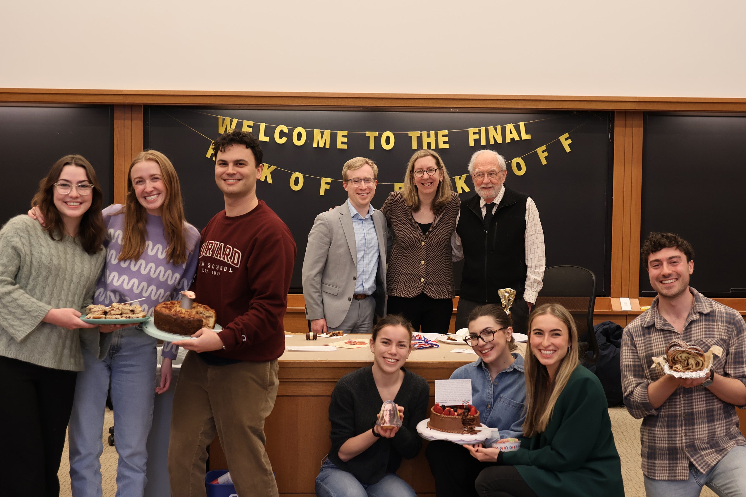 Several small groups pose in a classroom holding baked goods.