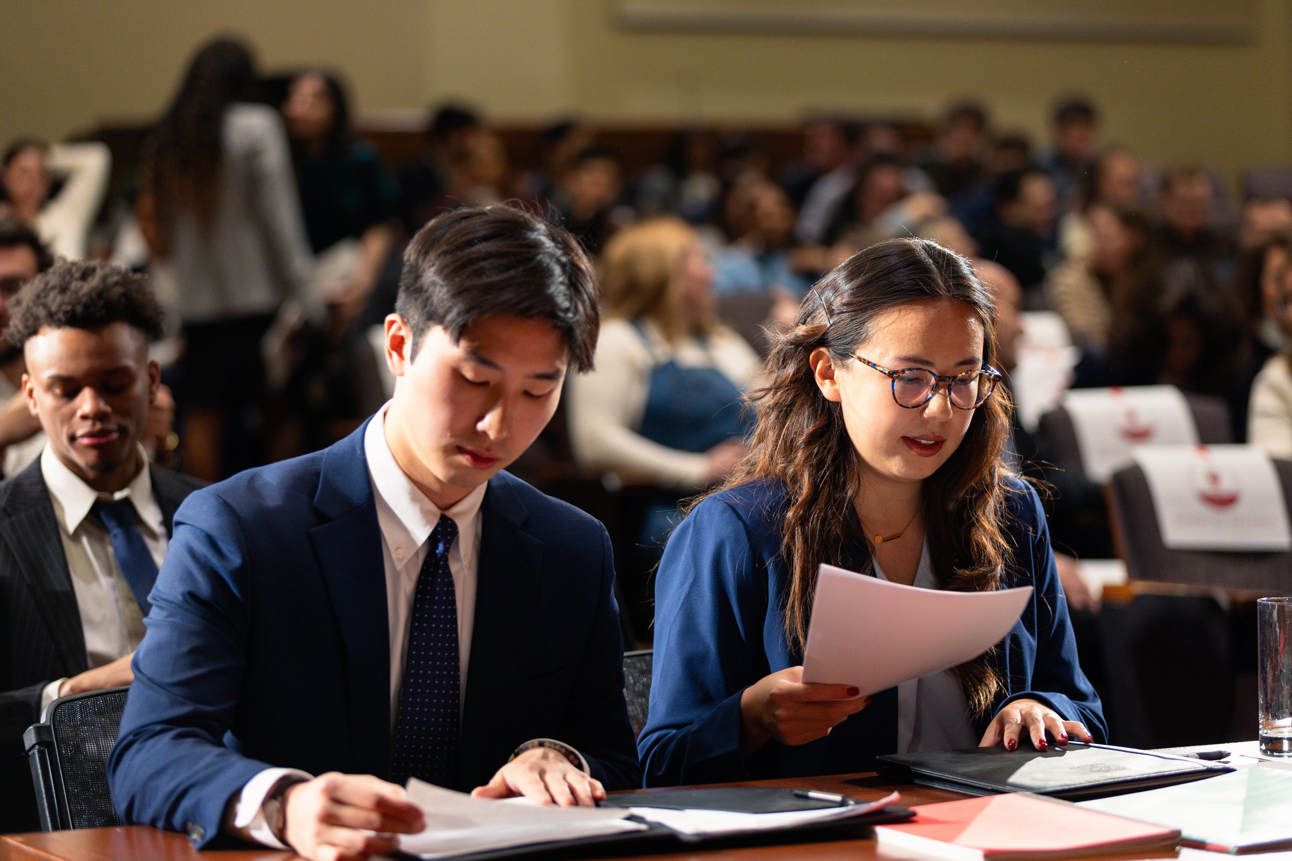 Two students look over papers on a desk in front of them.