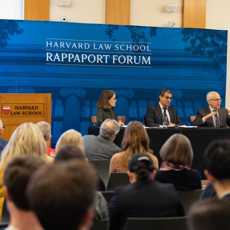 Panelists sit behind a table in front of a blue backdrop.