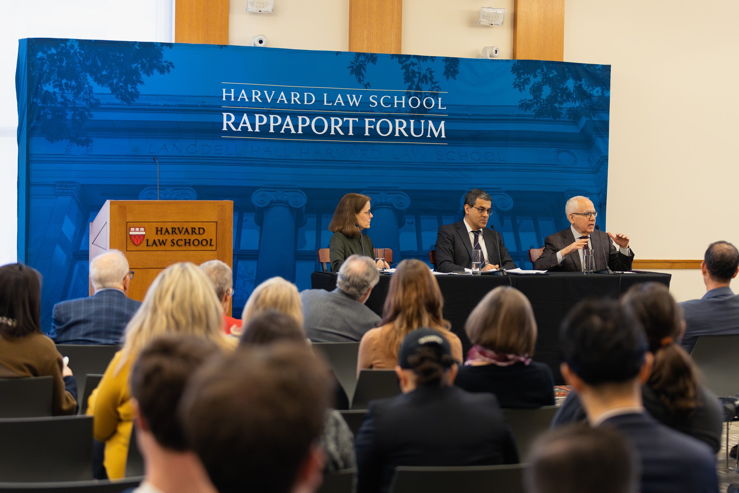 Panelists sit behind a table in front of a blue backdrop.