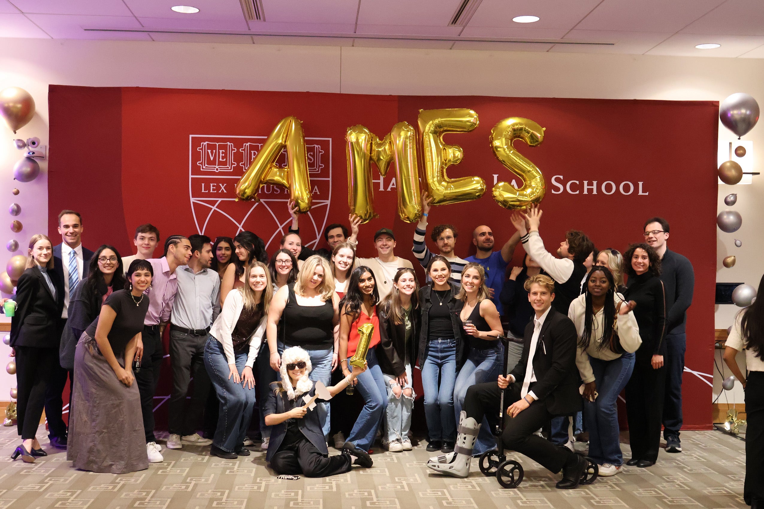 A crowd of students pose in front of a backdrop holding balloons which spell 