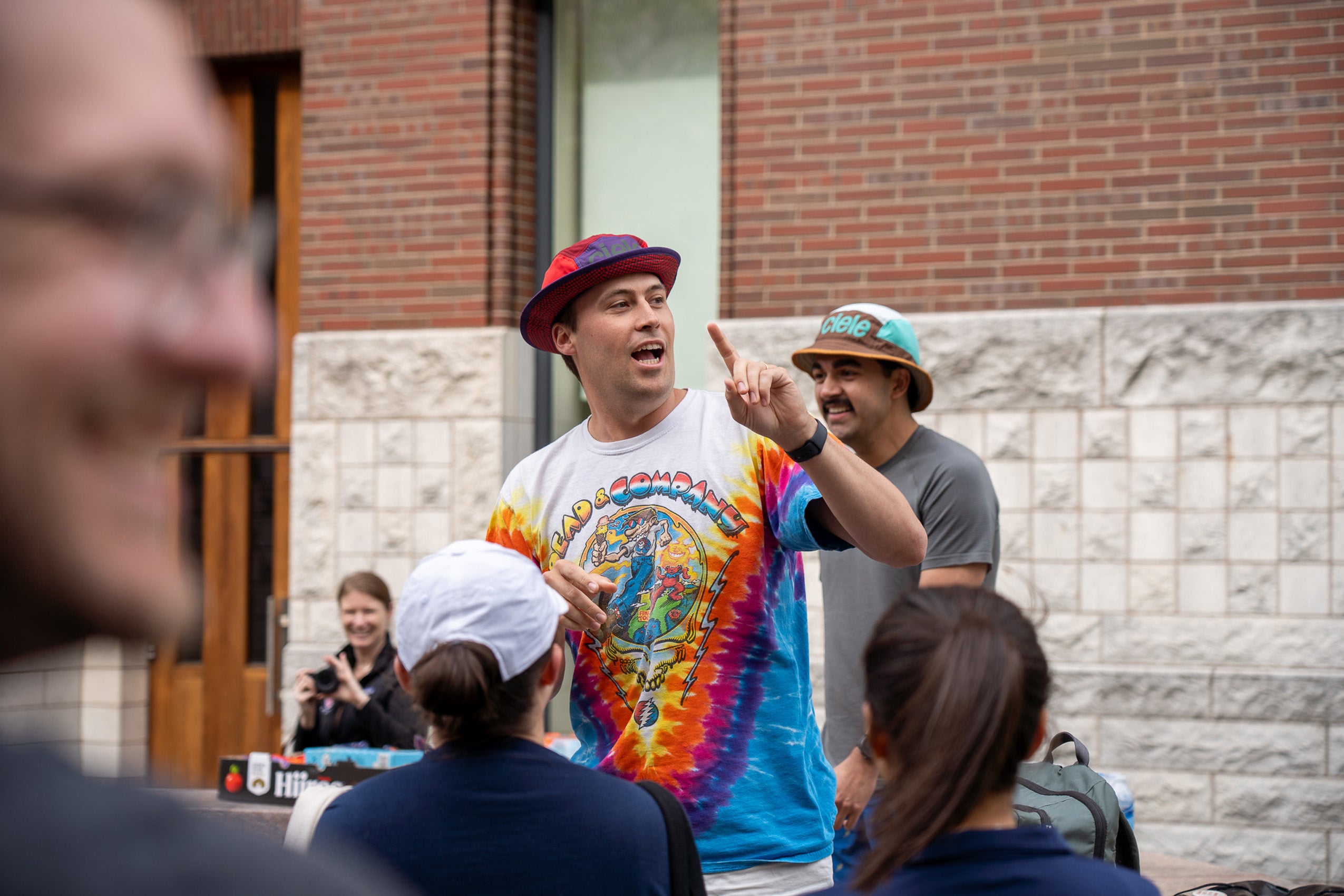 A man in a colorful t-shirt speaks to a crowd on campus