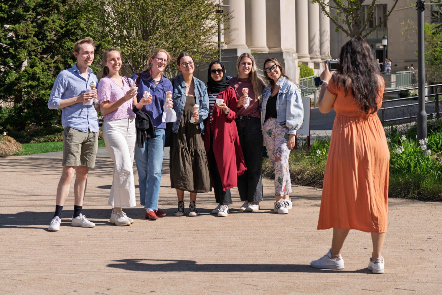 A line of students holding ice cream cones on campus pose for a cell phone photo.