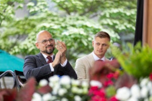 Two men sitting on stage. One man applauds