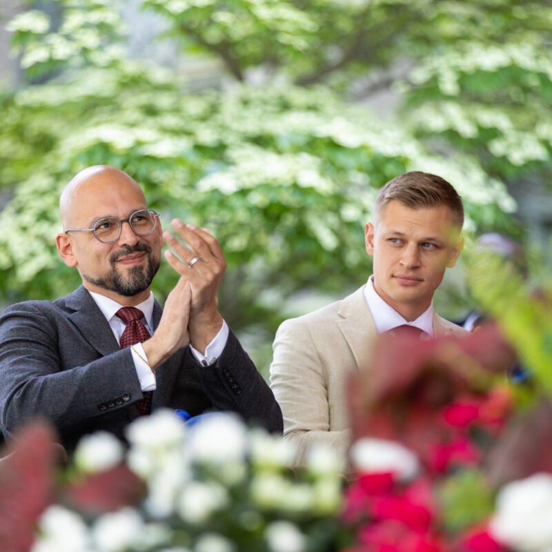 Two men sitting on stage. One man applauds