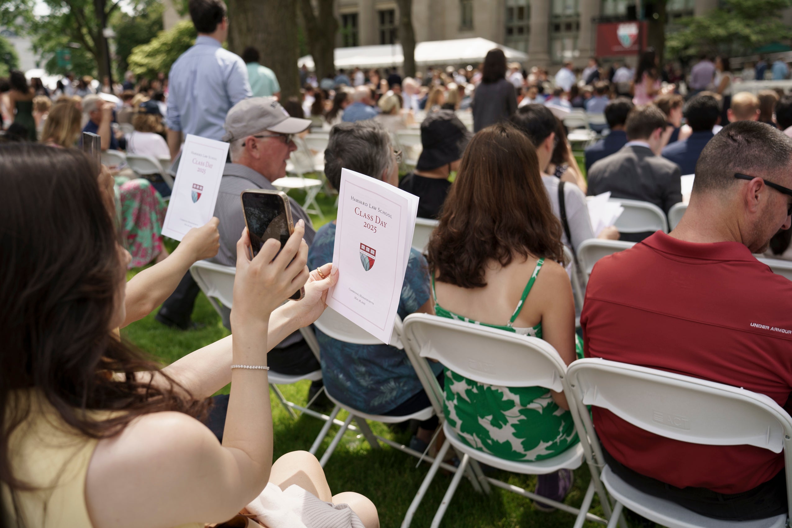 A woman takes a photo of her Class Day program