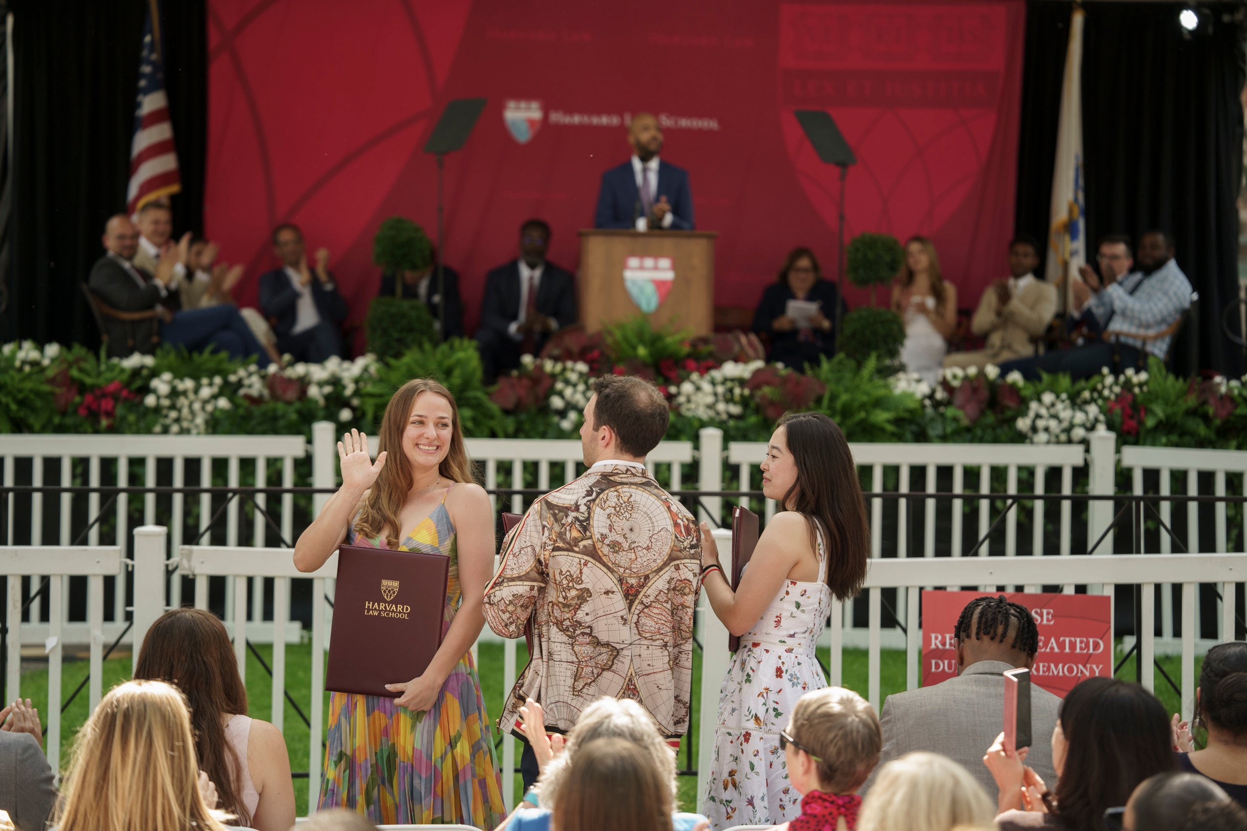 Three people standing in an audience. One woman holding an award waves