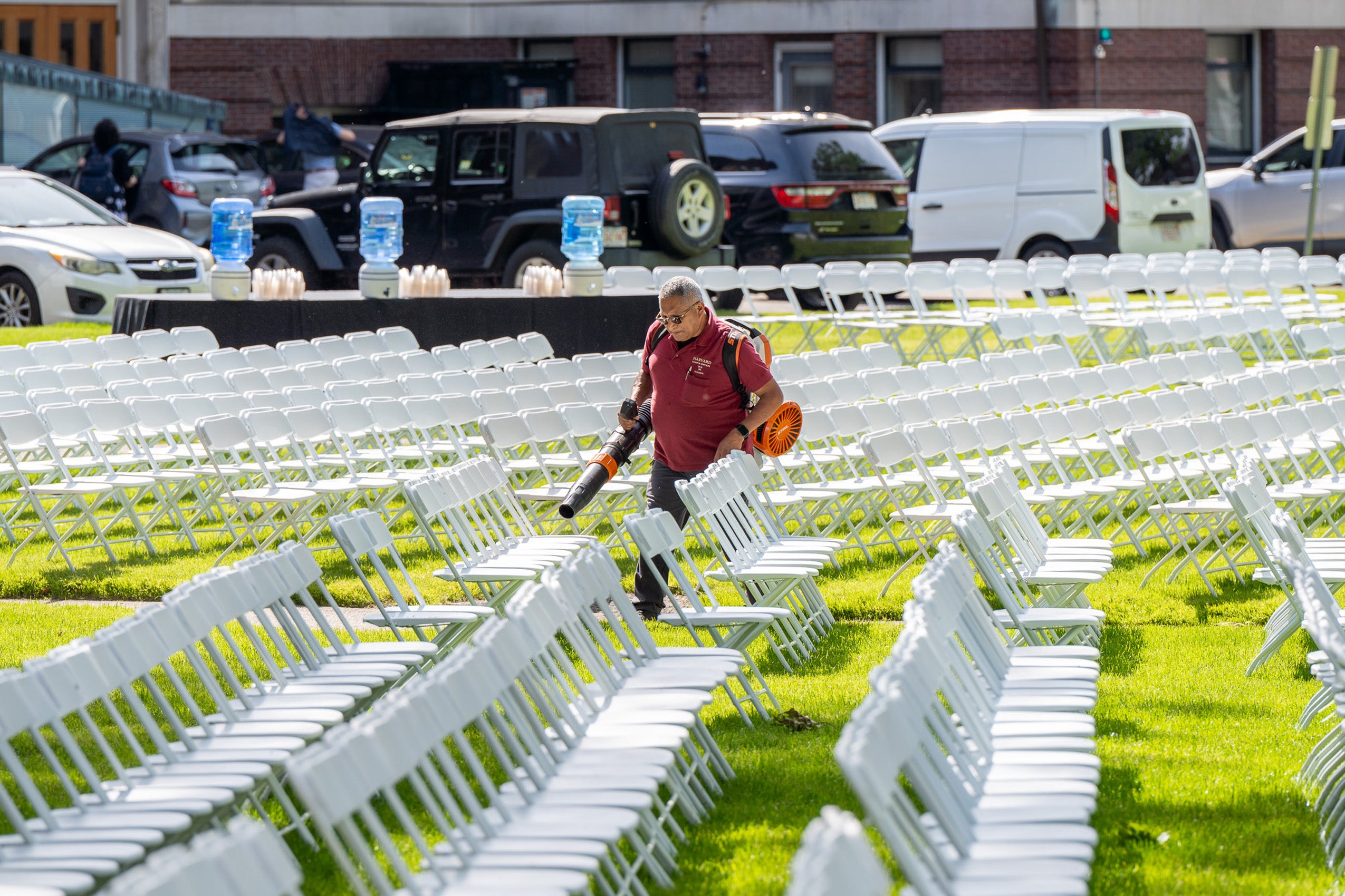 A man cleans rows of white chairs with a blower.