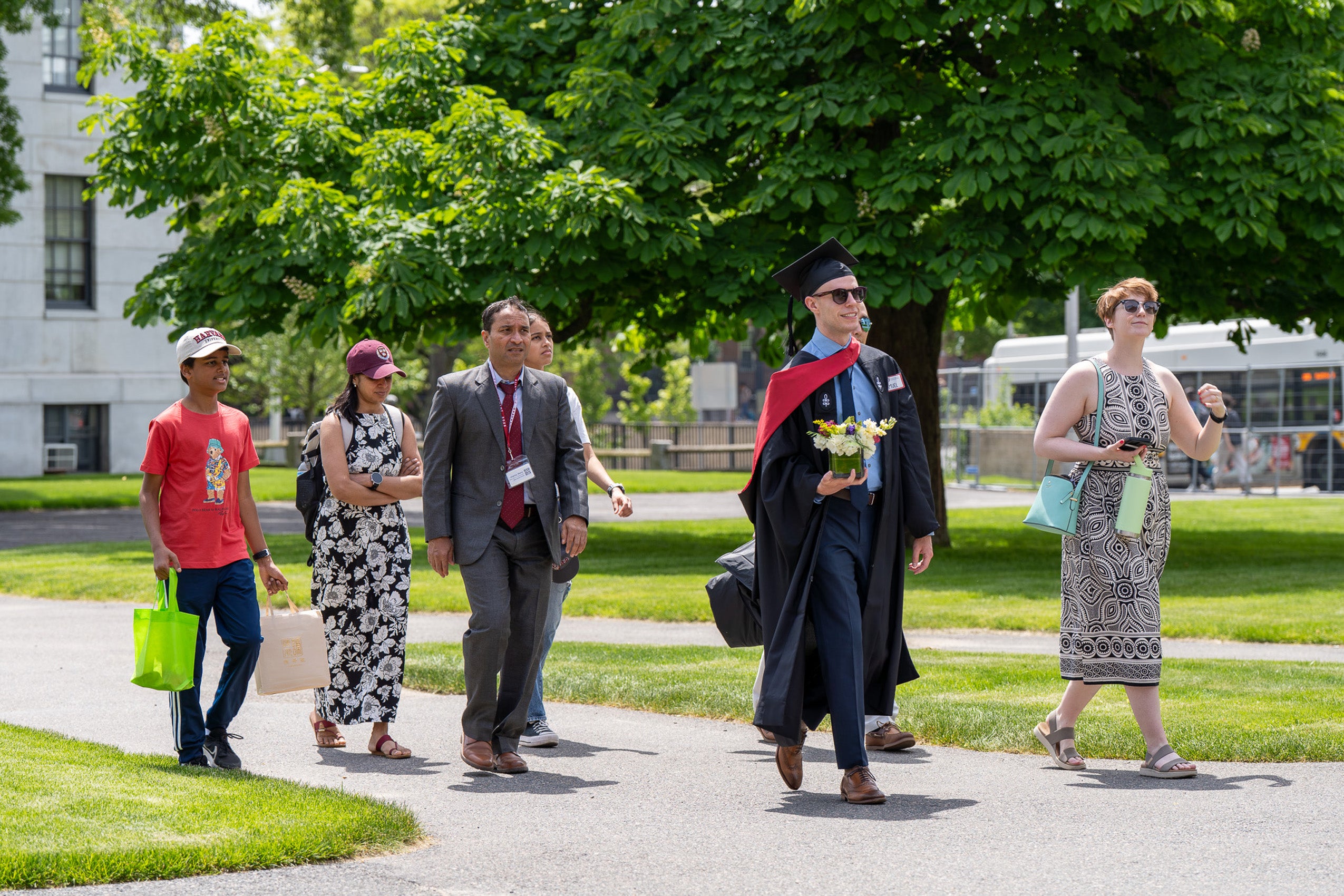 One person in commencement regalia walks along with others on a path on campus.