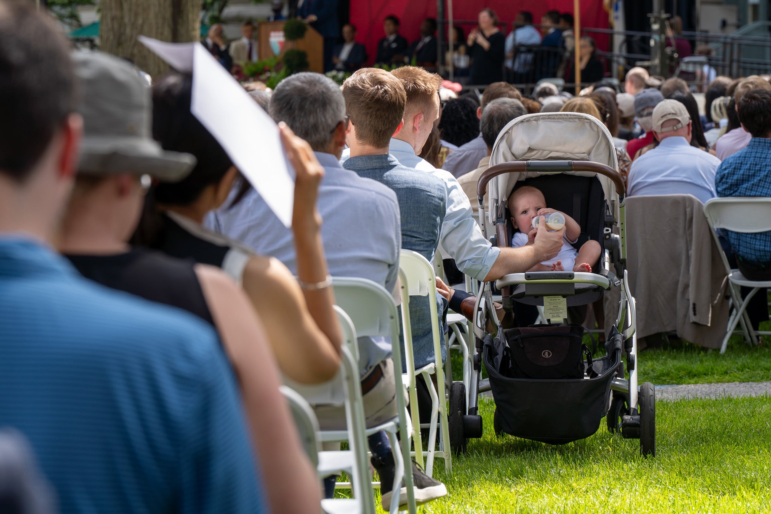 A man in the audience feeds a bottle to baby in a carriage.