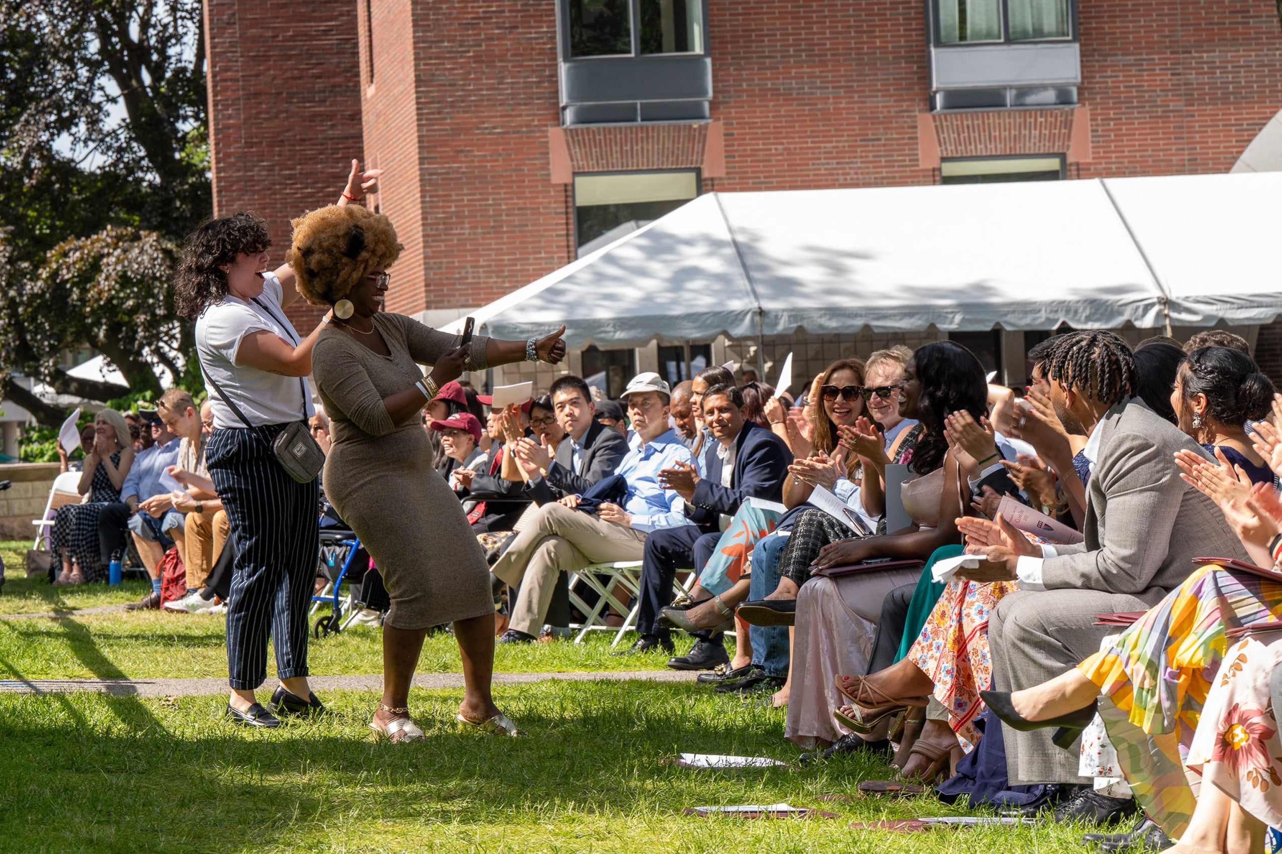 Two people take cell phone candids in front of an audience at an event.