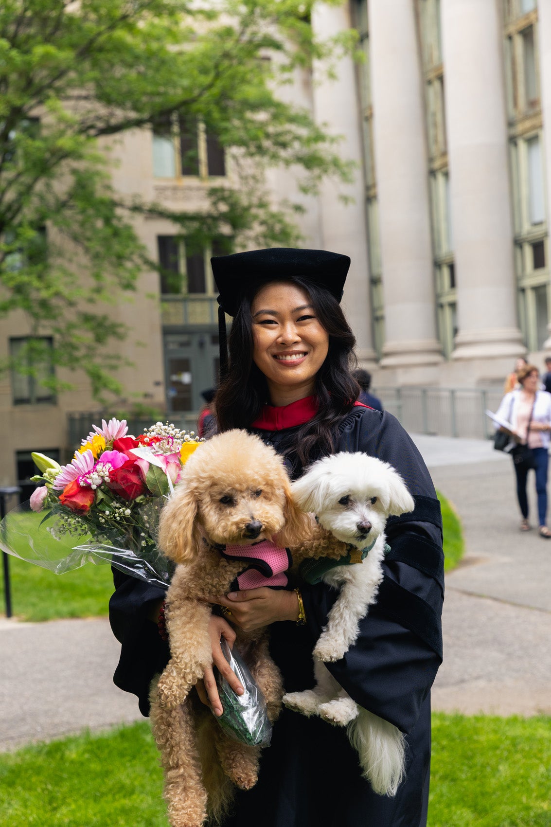 A graduate smiling and holding two dogs