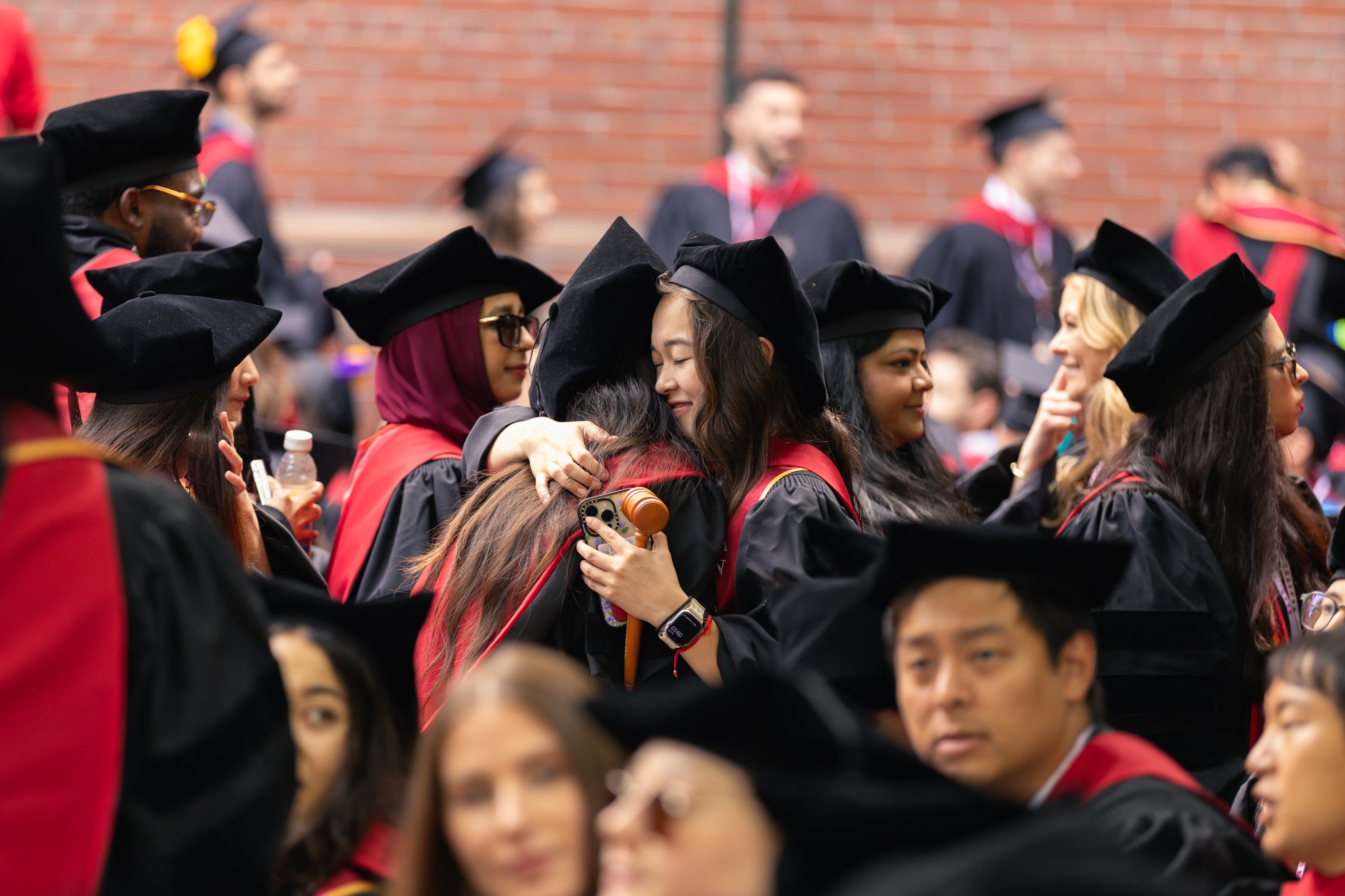 Two graduates hugging, surrounded by other graduates