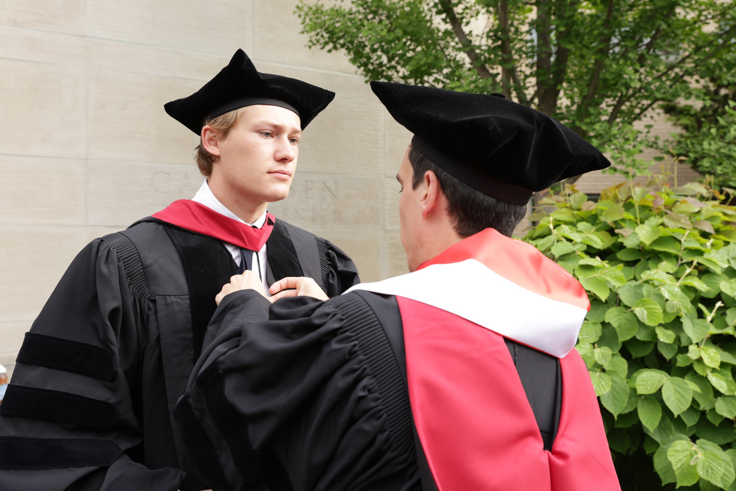 A graduate helping another graduate with his regalia