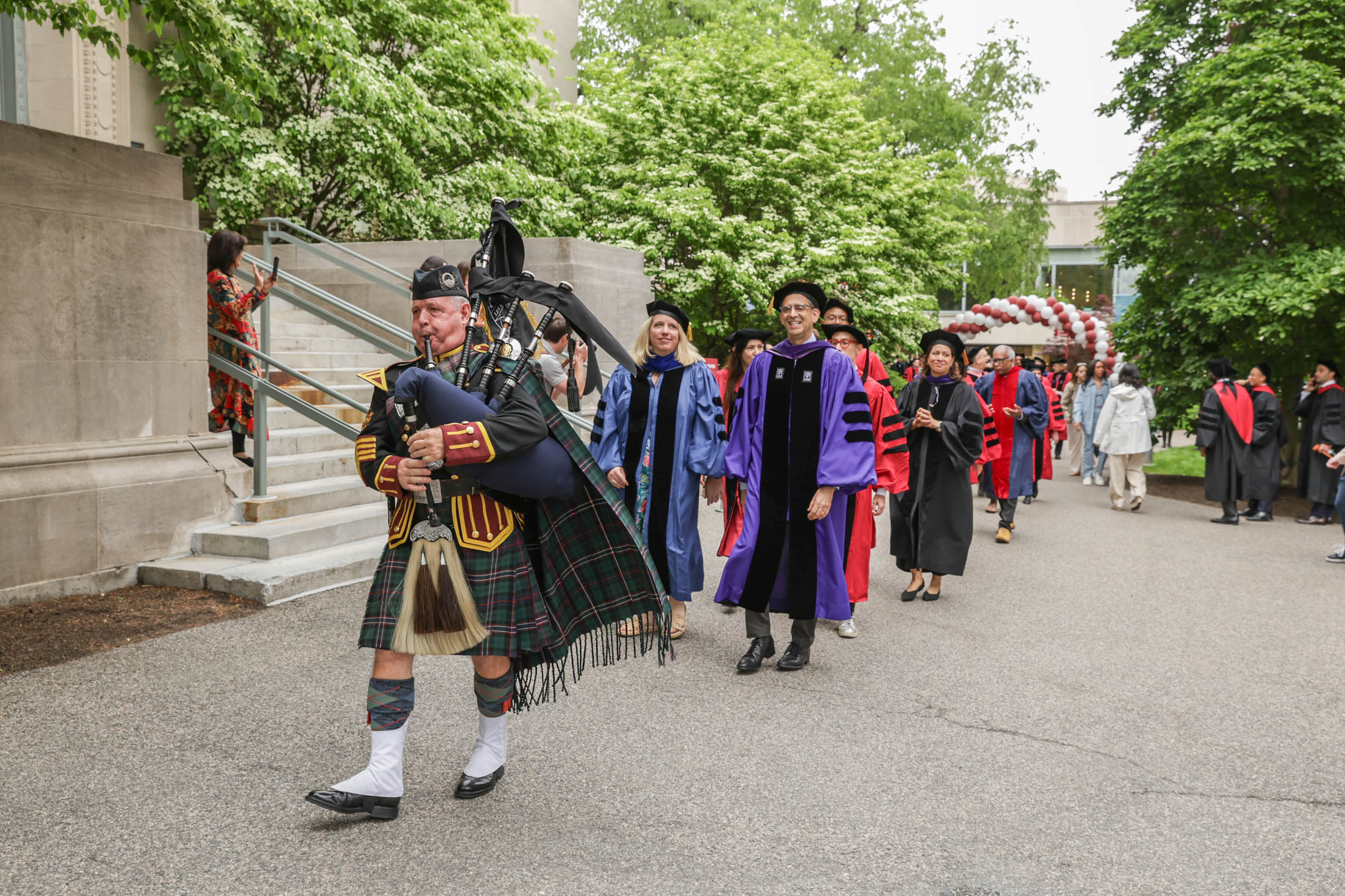 Harvard Law School Faculty walk in procession behind a bagpipe player.