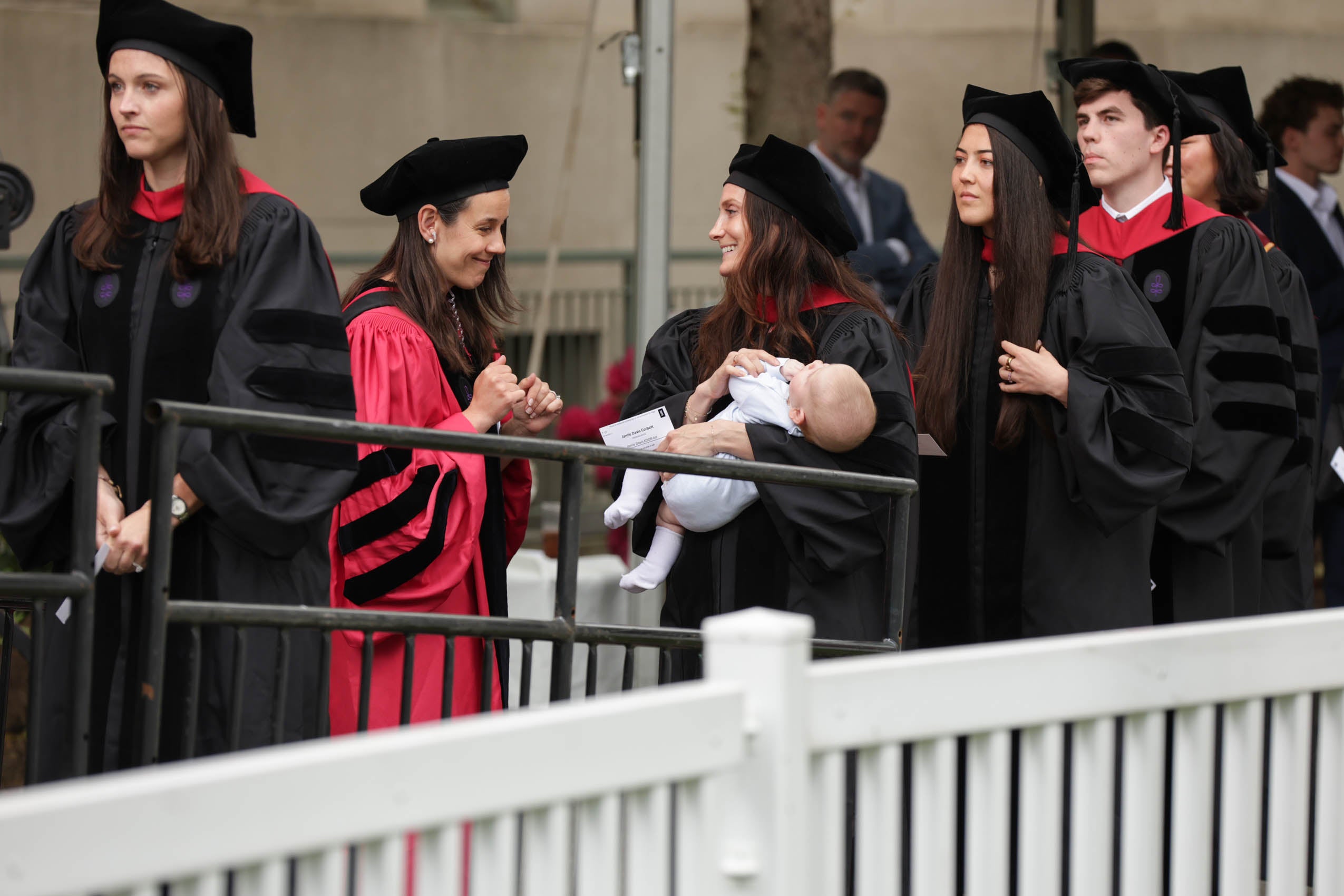 A graduate holding her baby standing in line to receive her diploma