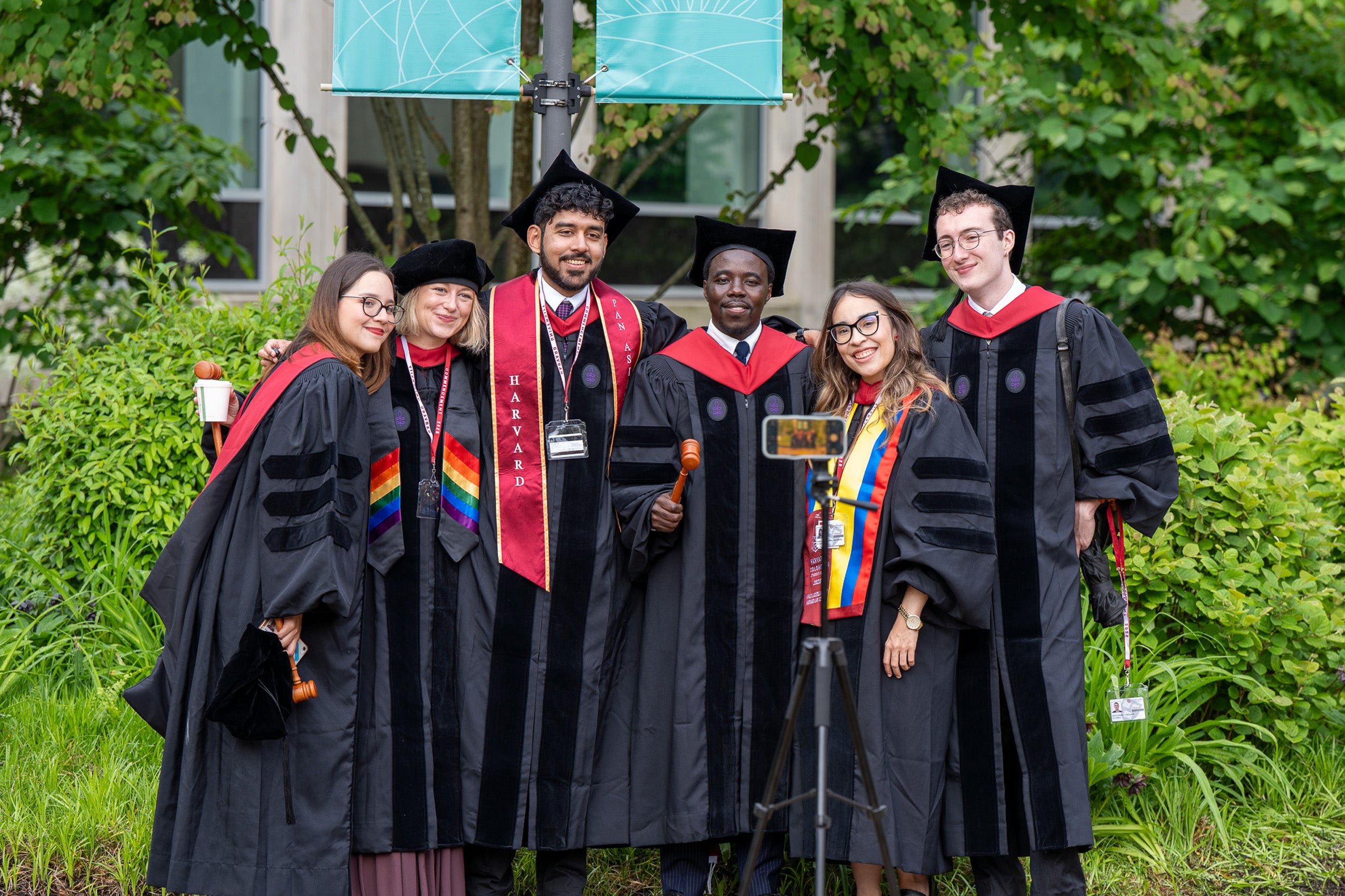 Six graduates pose in front of a cell phone on a tripod.