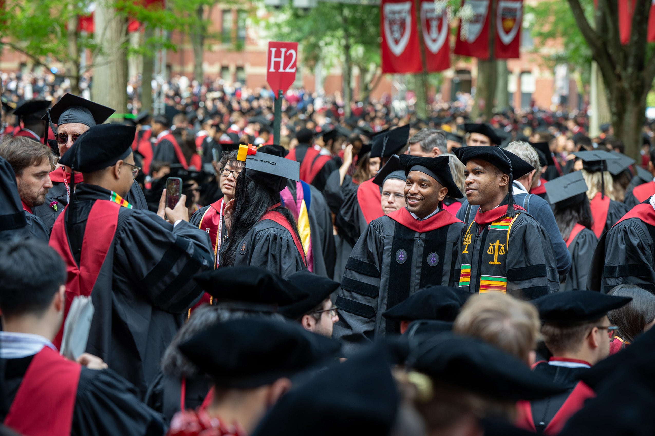 Two graduates pose for a photo in an area filled with other graduates.