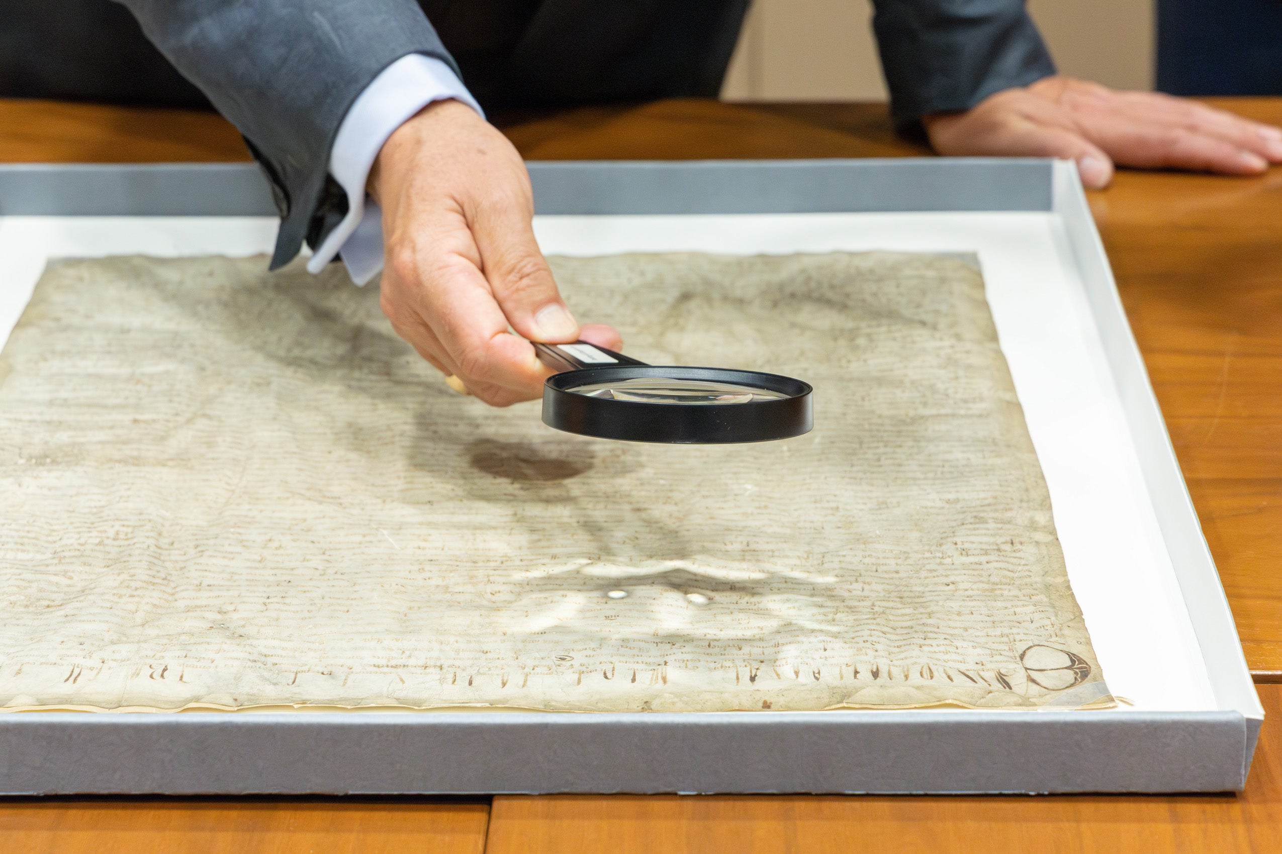 A researcher holds a magnifying glass over a portion of the Magna Carta.