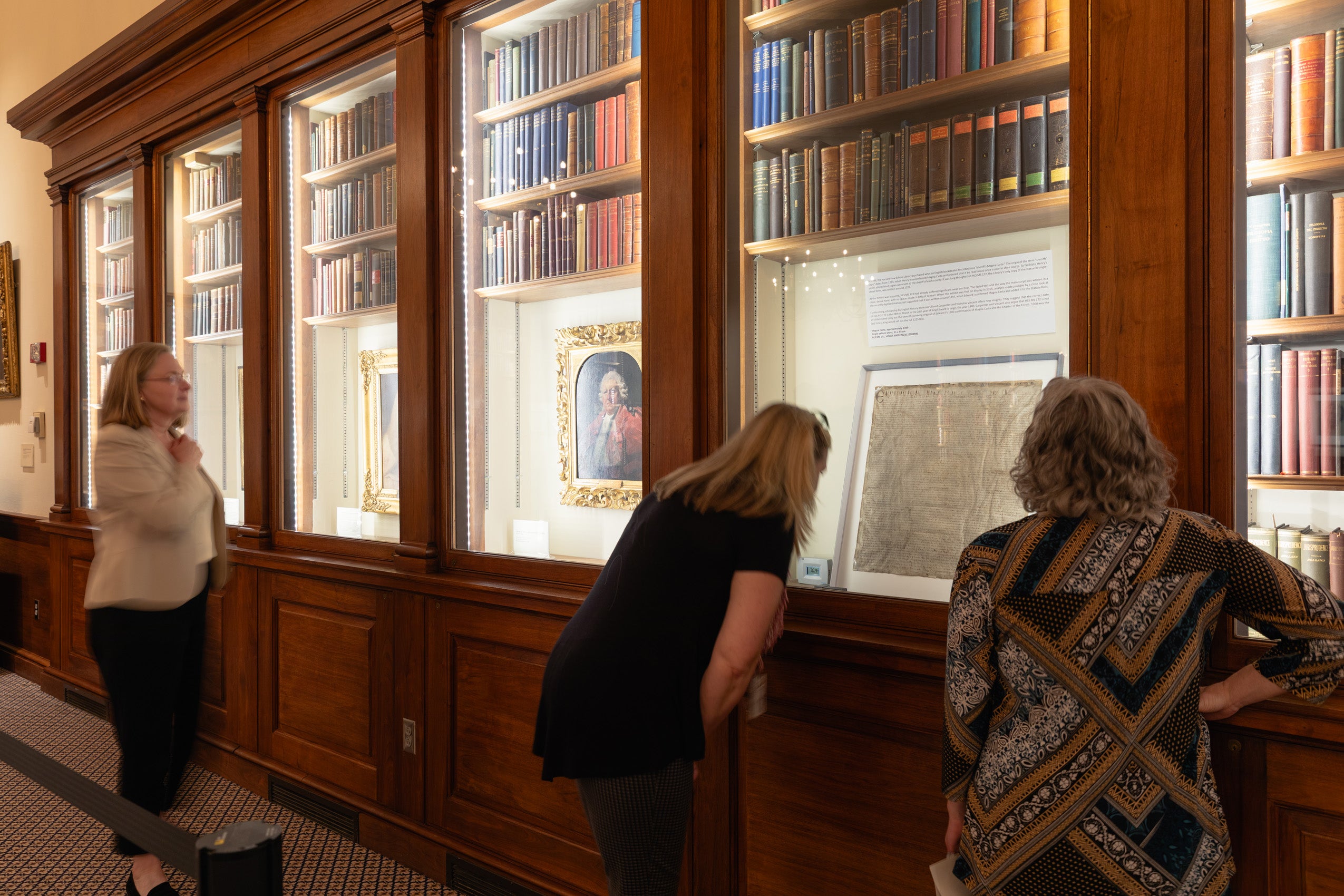 Three people look at documents and other items in a glass display case.