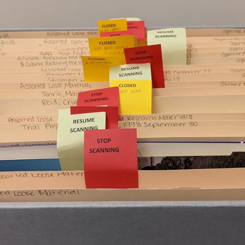 An open box containing 19 folders. Several flags are inserted into the folders with various typed phrases: “stop scanning,” “resume scanning,” and “closed.”