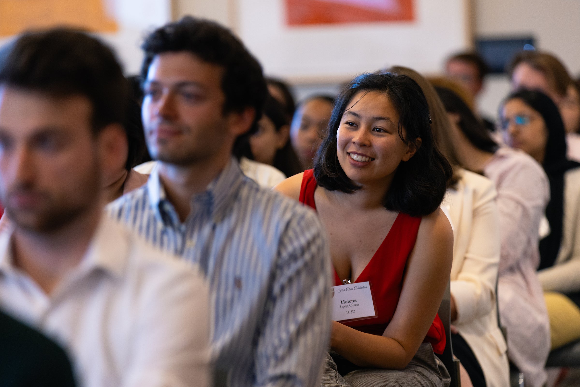 A student sitting in the audience smiles as she listens to remarks.