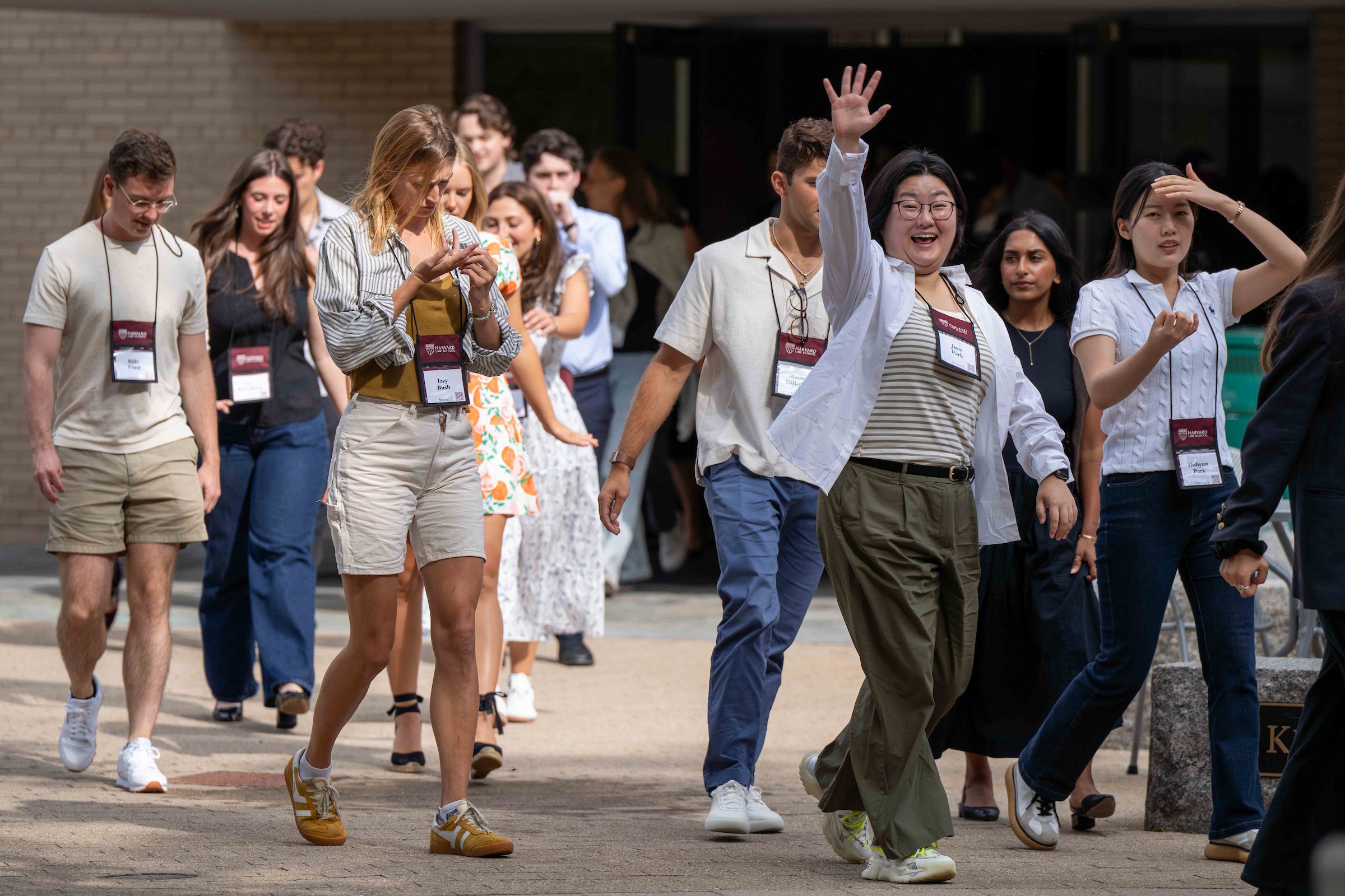 Student waves enthusiastically as she walks with her classmates to Sanders Theatre.