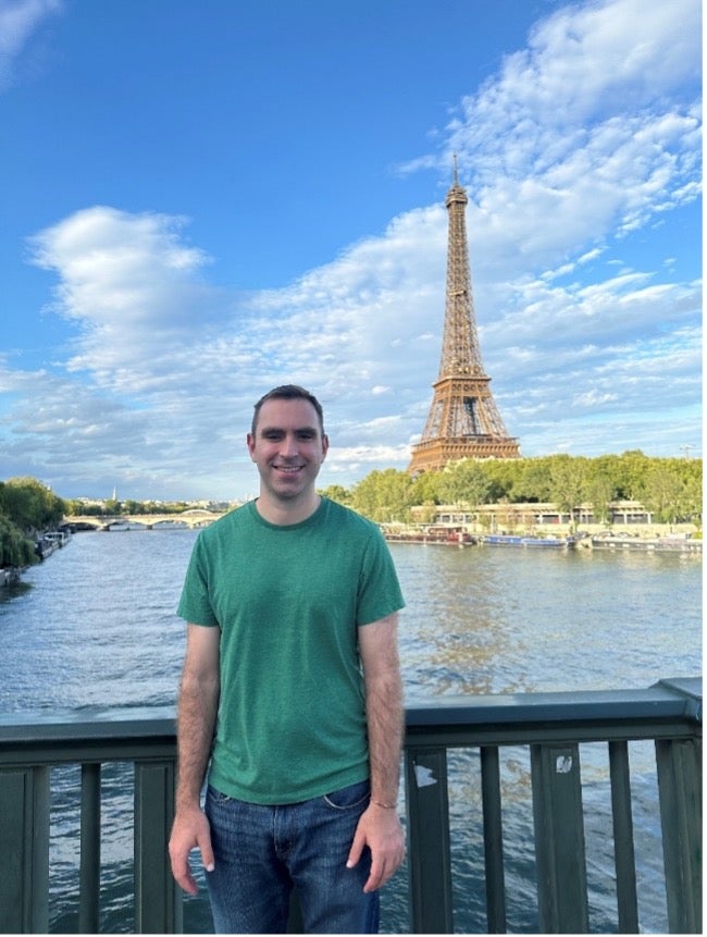 Man standing on bridge with Eiffel Tower in background.