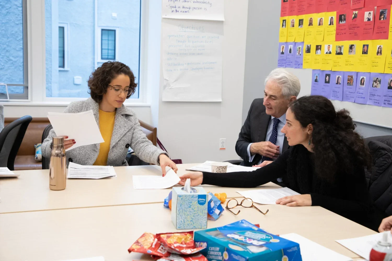 Three people gathered around a table exchanging papers.