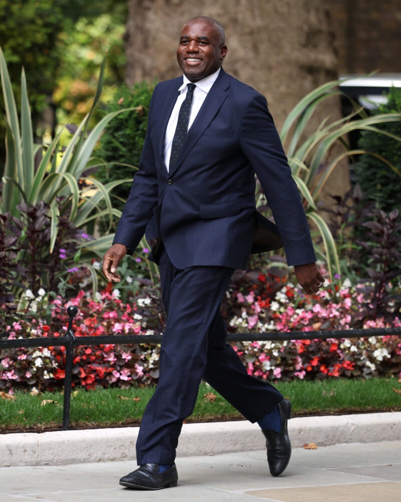 David Lammy walking on a path lined with flowers.
