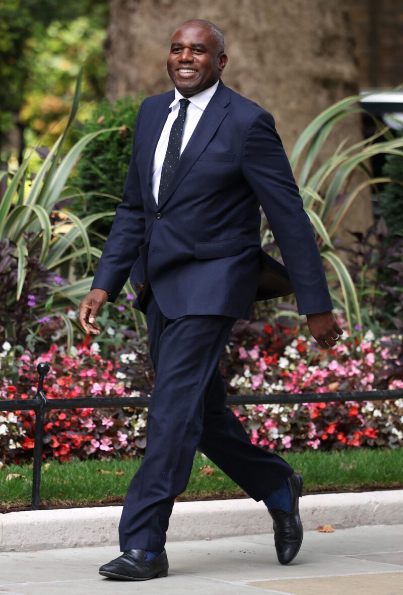 David Lammy walking on a path lined with flowers.