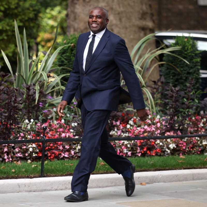 David Lammy walking on a path lined with flowers.