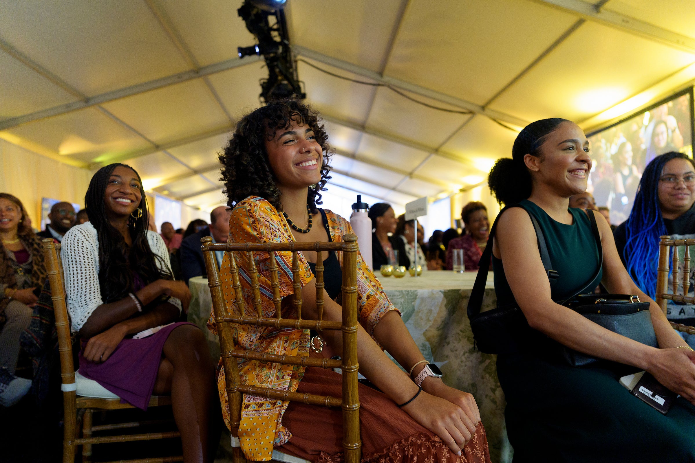 Several people sitting at tables listen to a talk at an event.