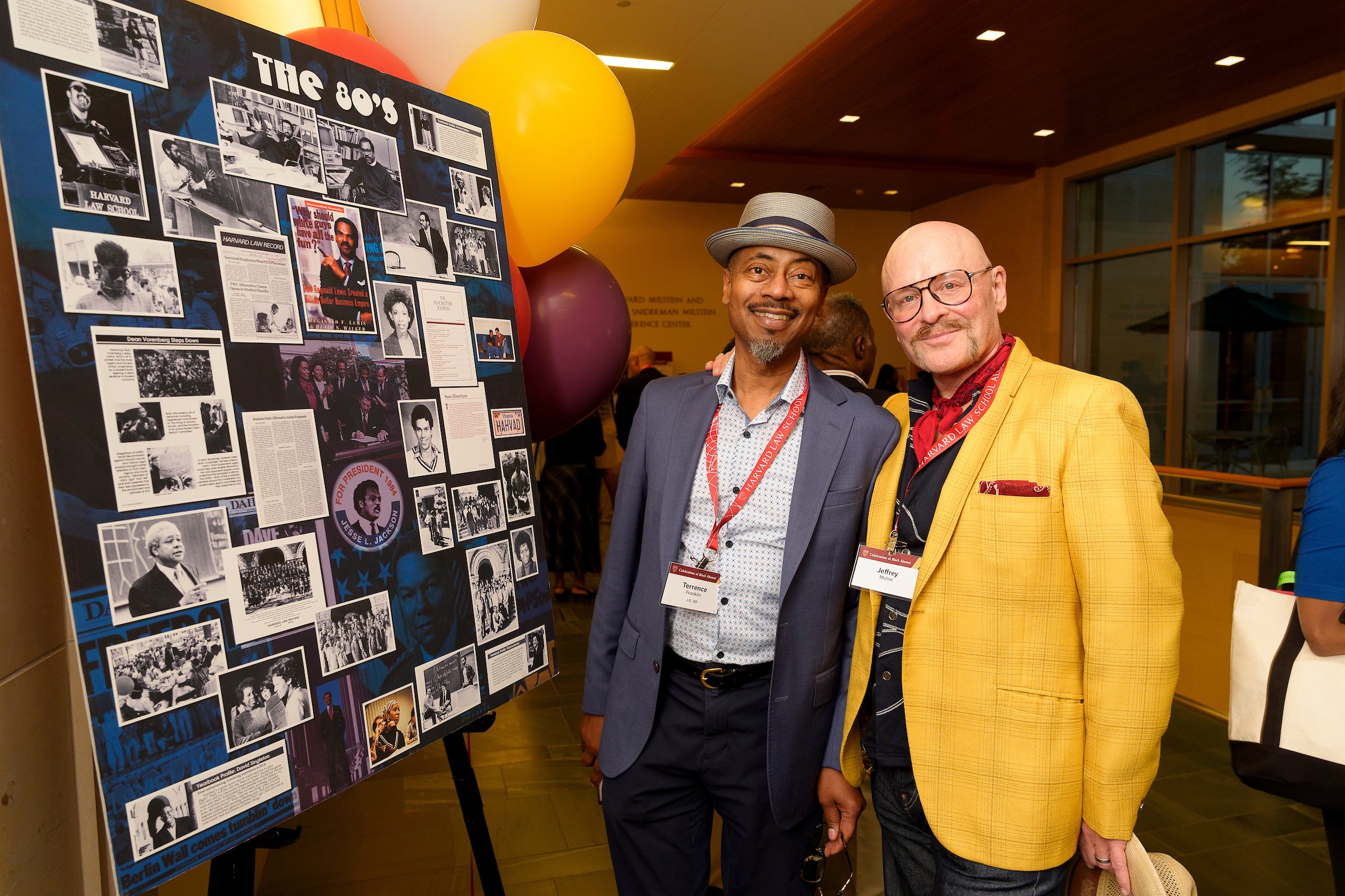 Two men standing in front of a collection of photos on a poster.