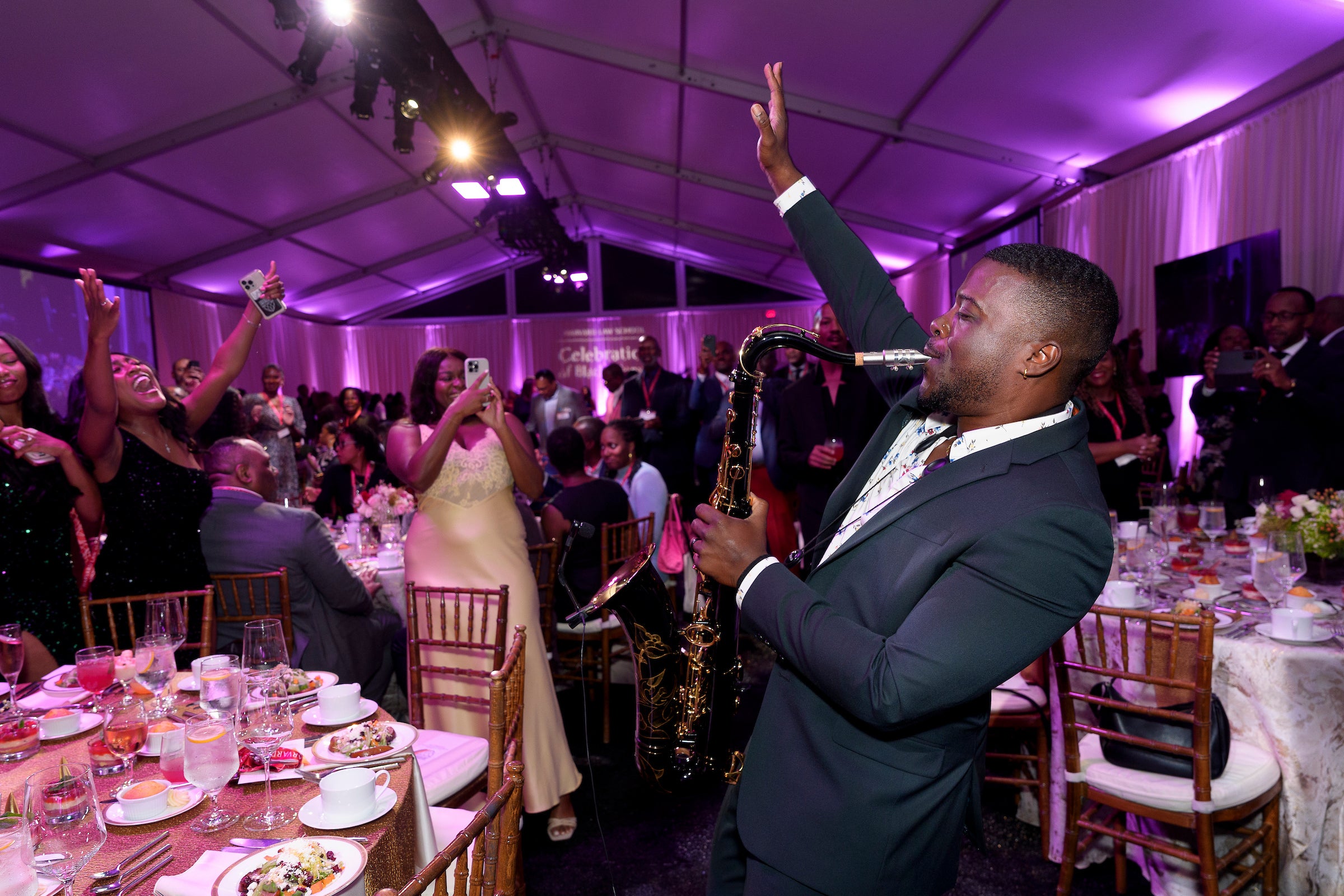 A saxophone player plays to a group of people gathered at a celebratory event.