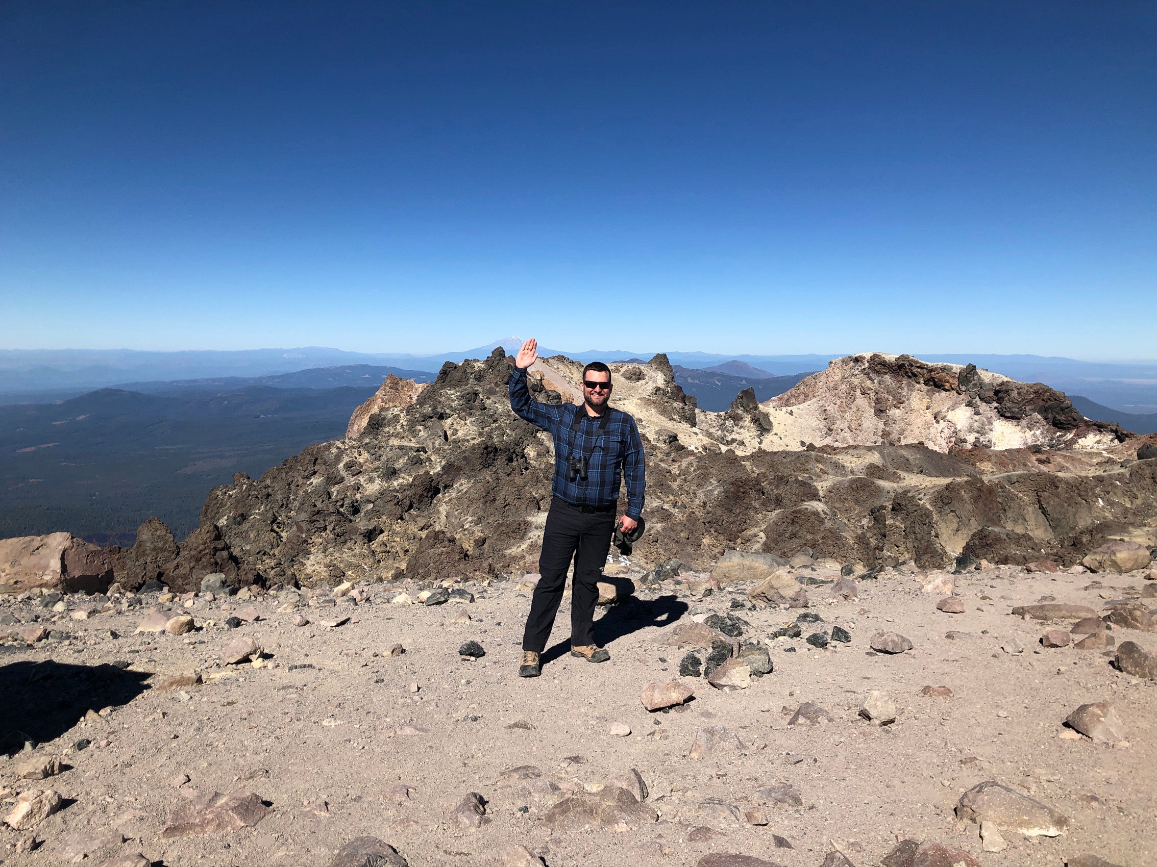 A man standing at the top of a mountain waves.