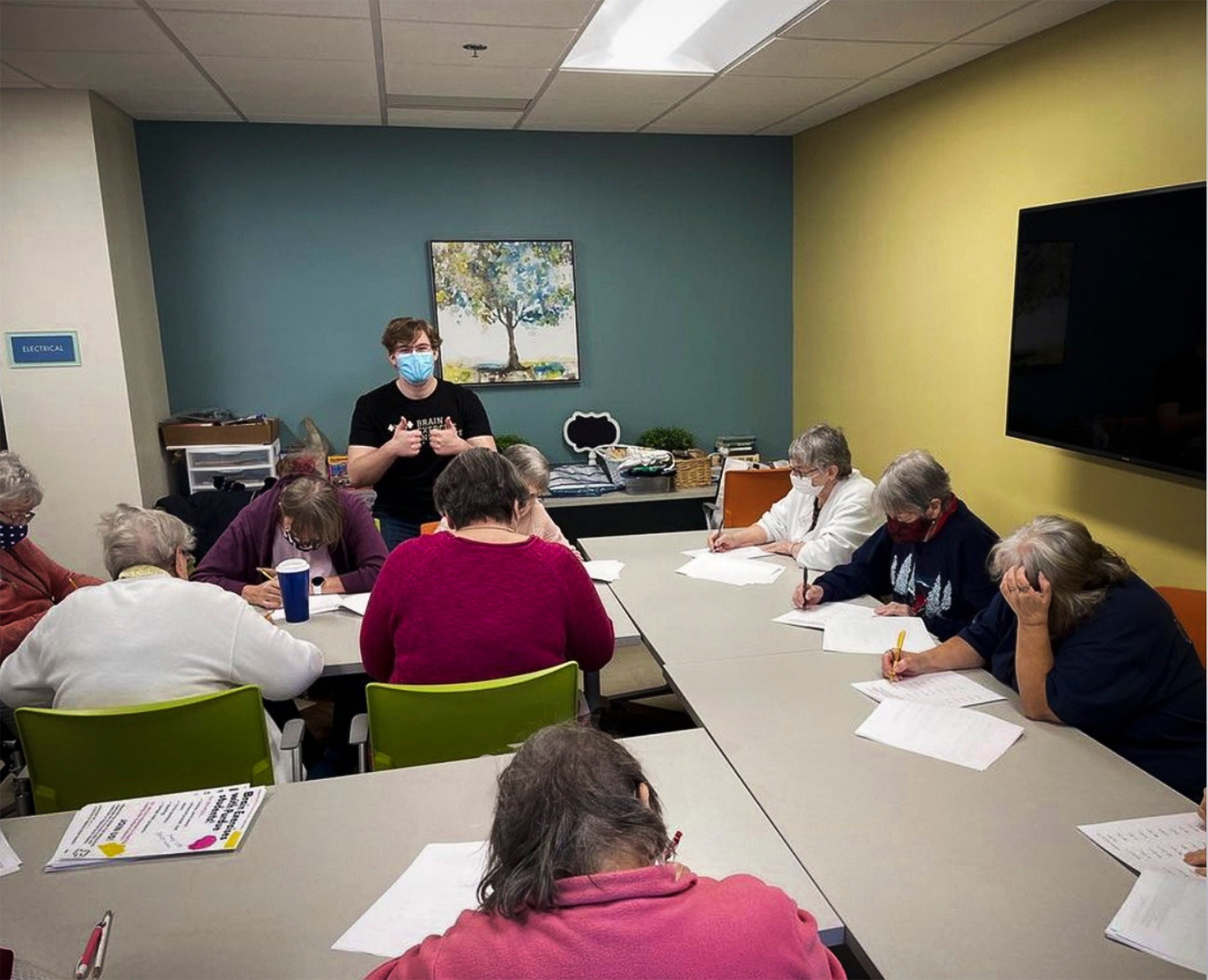 A classroom of older people doing paperwork as someone teaches.