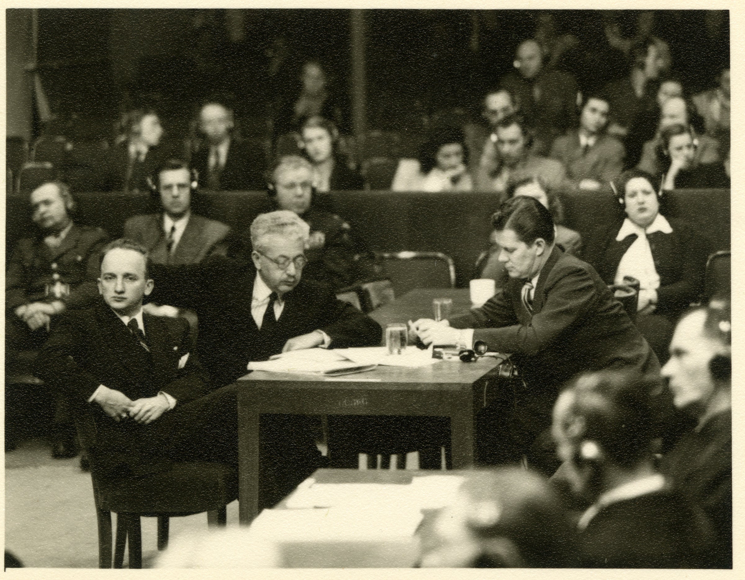 Ben Ferencz seated at a table with two others during the Einsatzgruppen trial at Nuremberg.