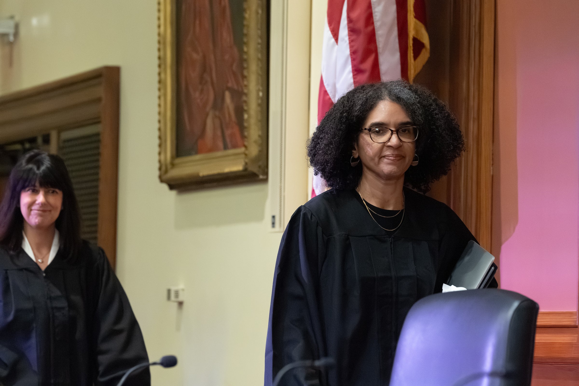 Two women in judges robes walk toward the bench in a courtroom.
