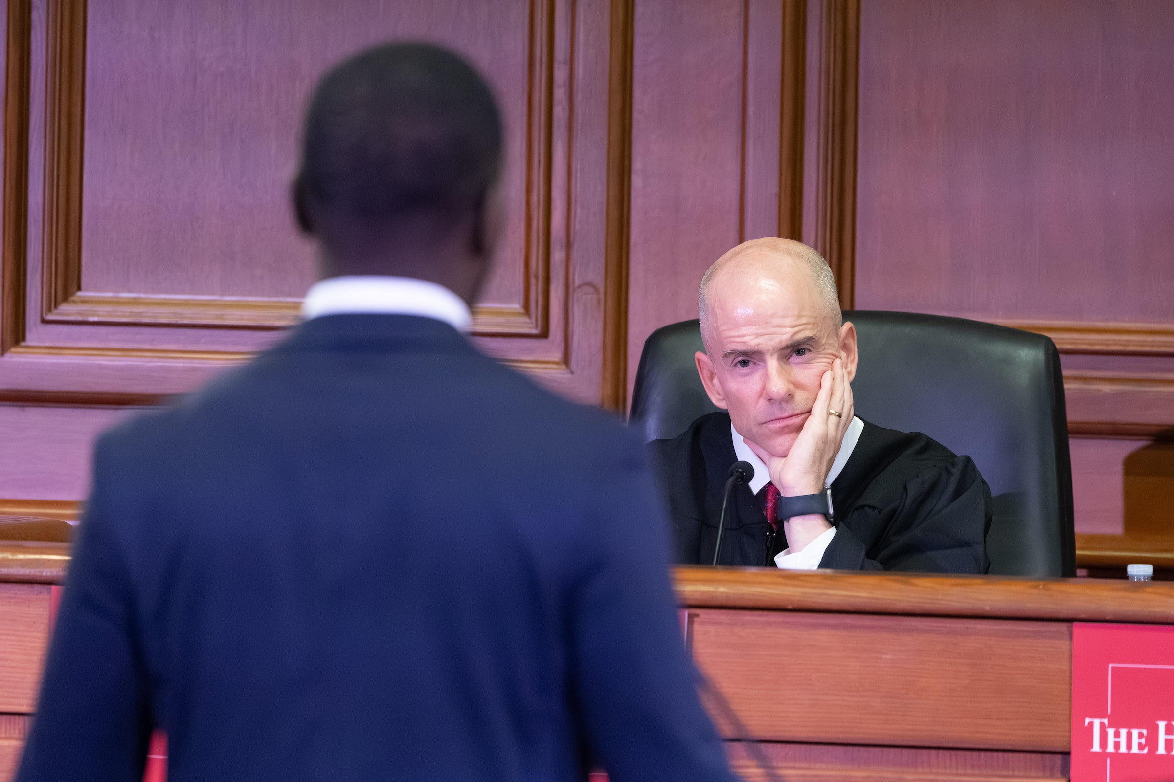 A man standing at a podium speaks to a judge.