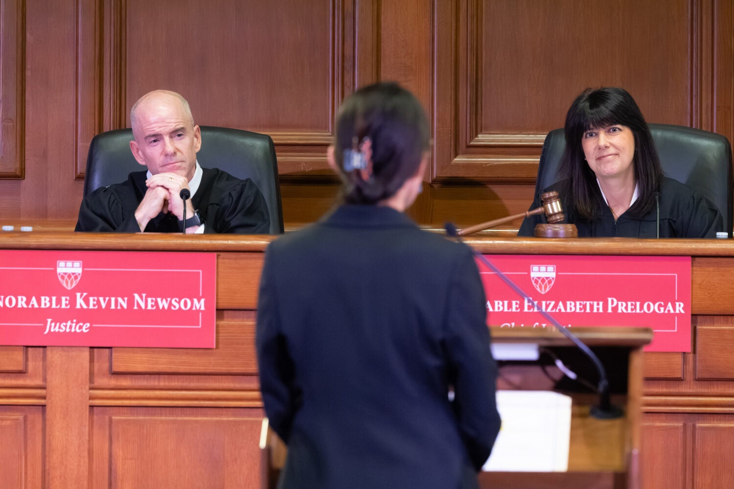 A woman at a podium in a courtroom in front of a bench with two judges.
