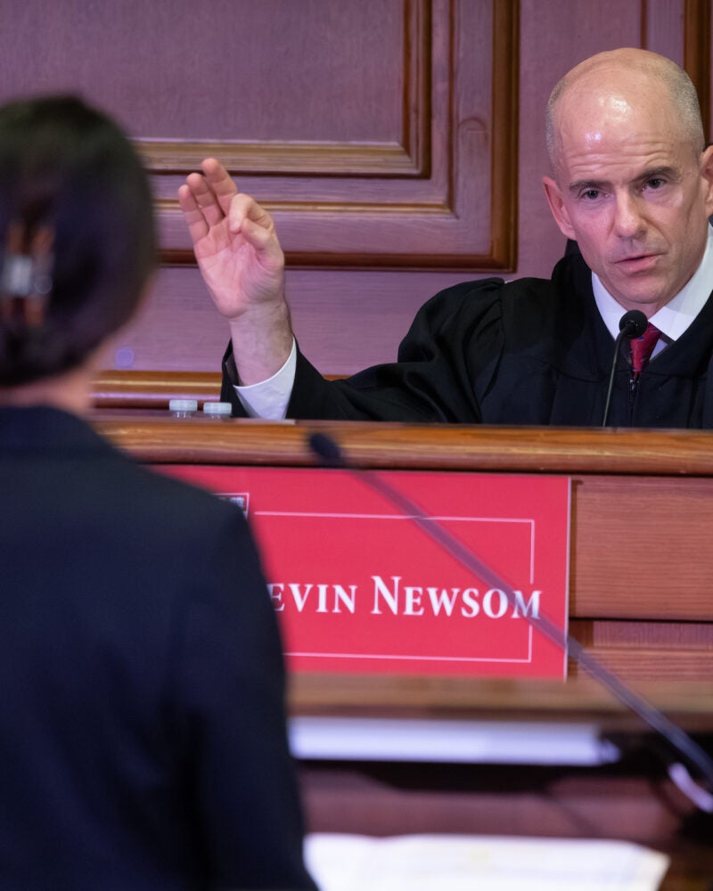 A woman stands at a podium as she speaks to a judge on the bench.