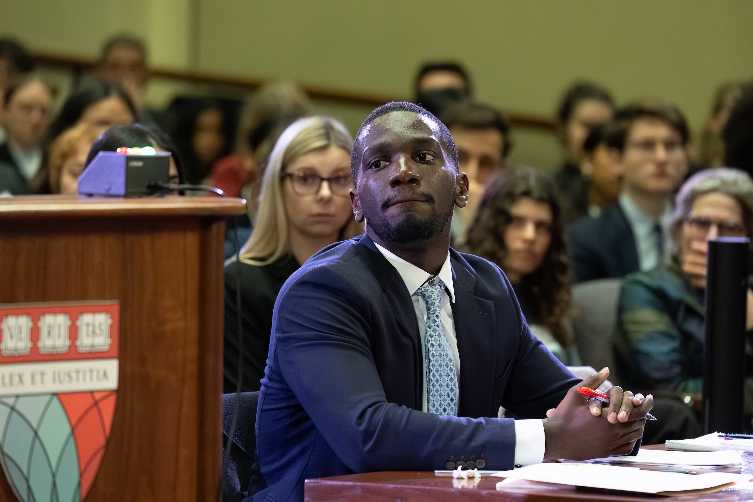 A man looks pensive as he is sitting at a table next to a podium.