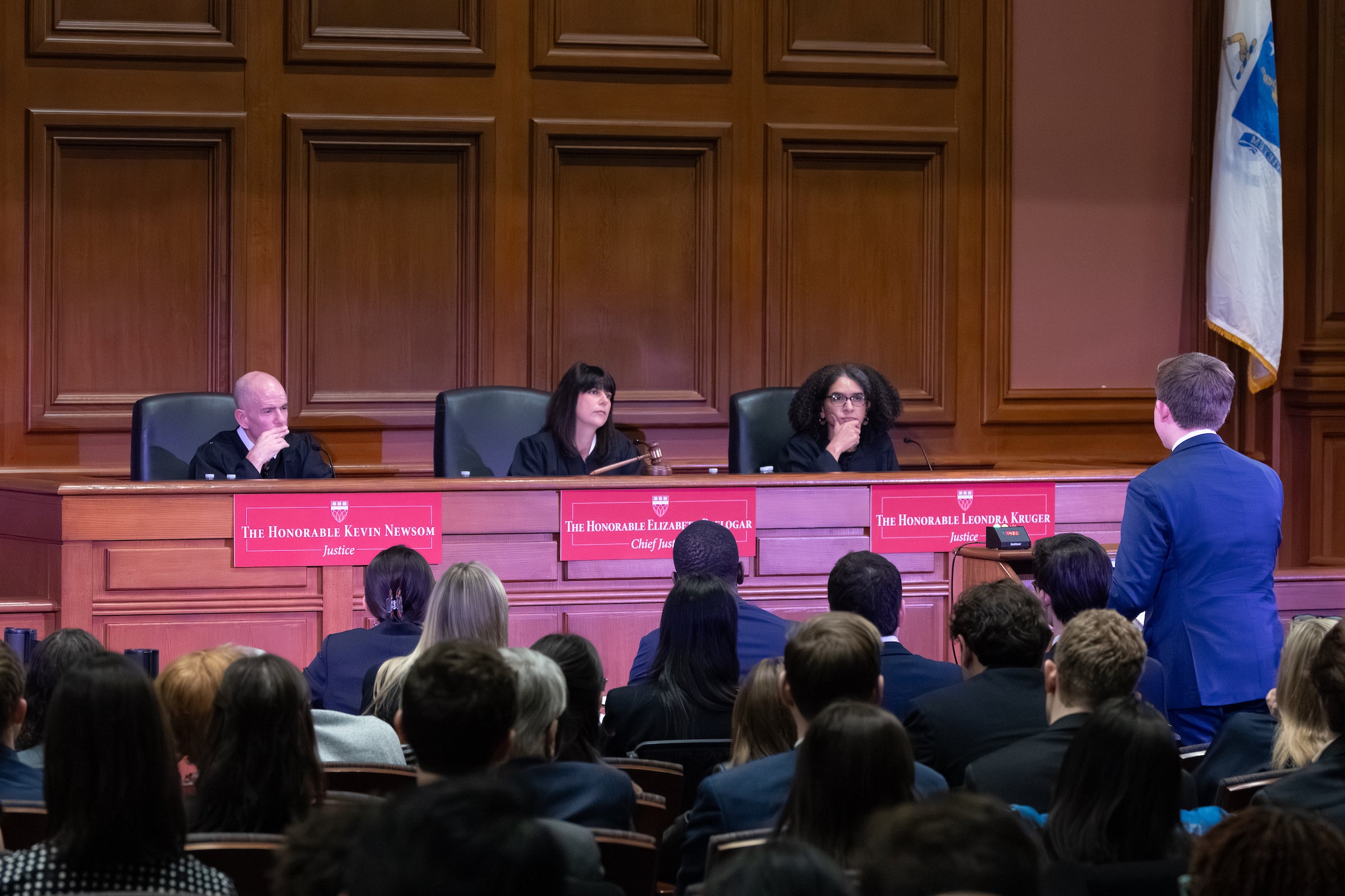 A man stands at a podium in a courtroombefore a panel of three judges.