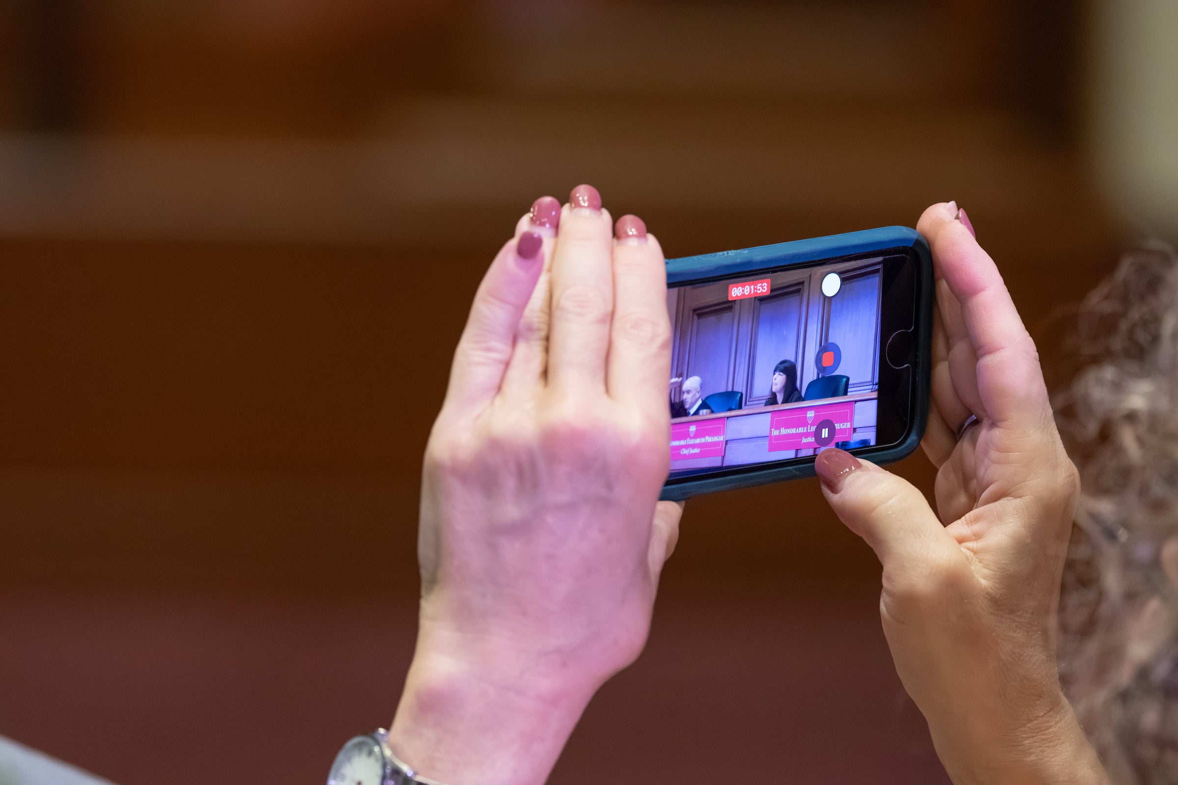 A cell phone capturing the judges is held up by two hands.