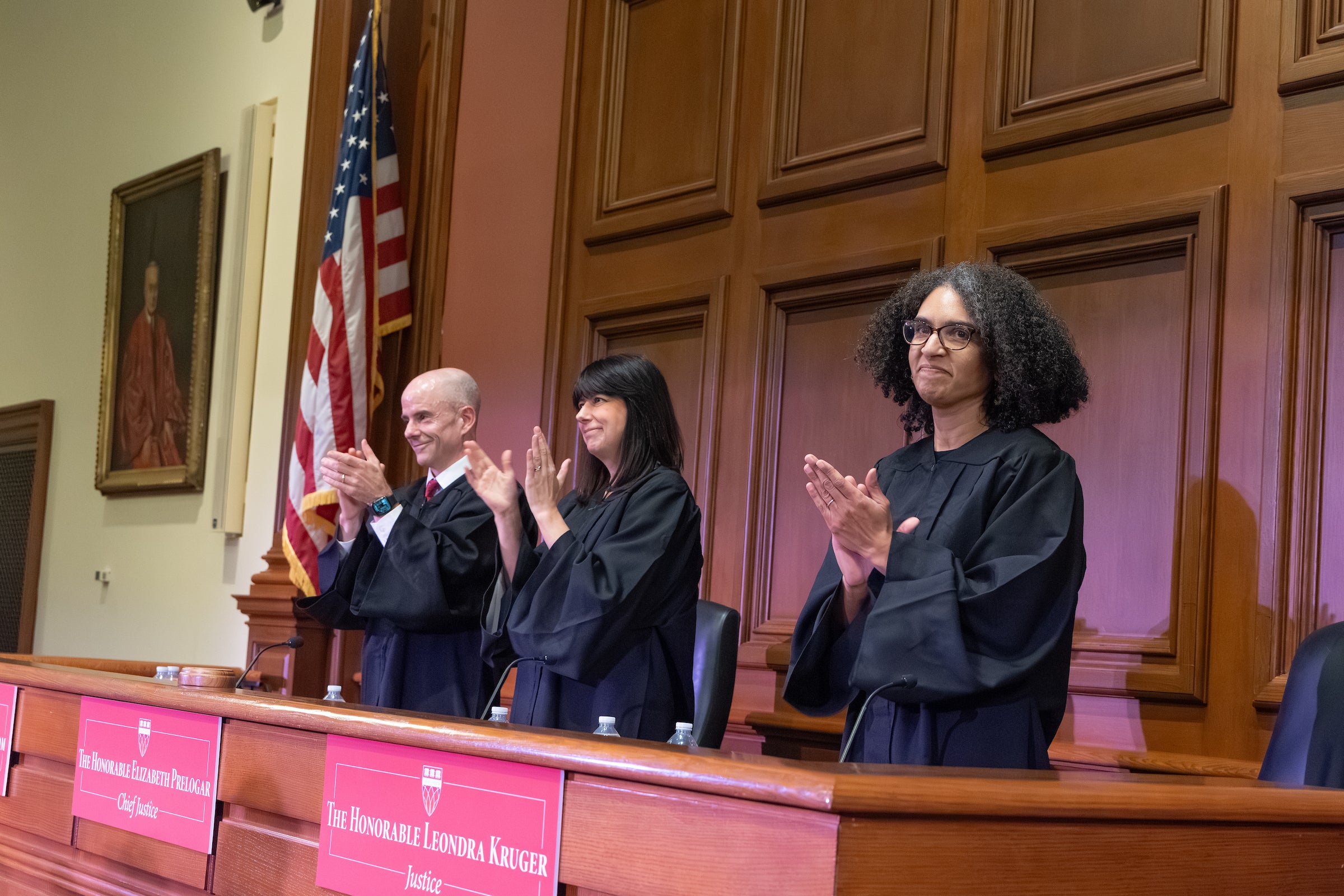 Three judges stand behind the bench and clap.