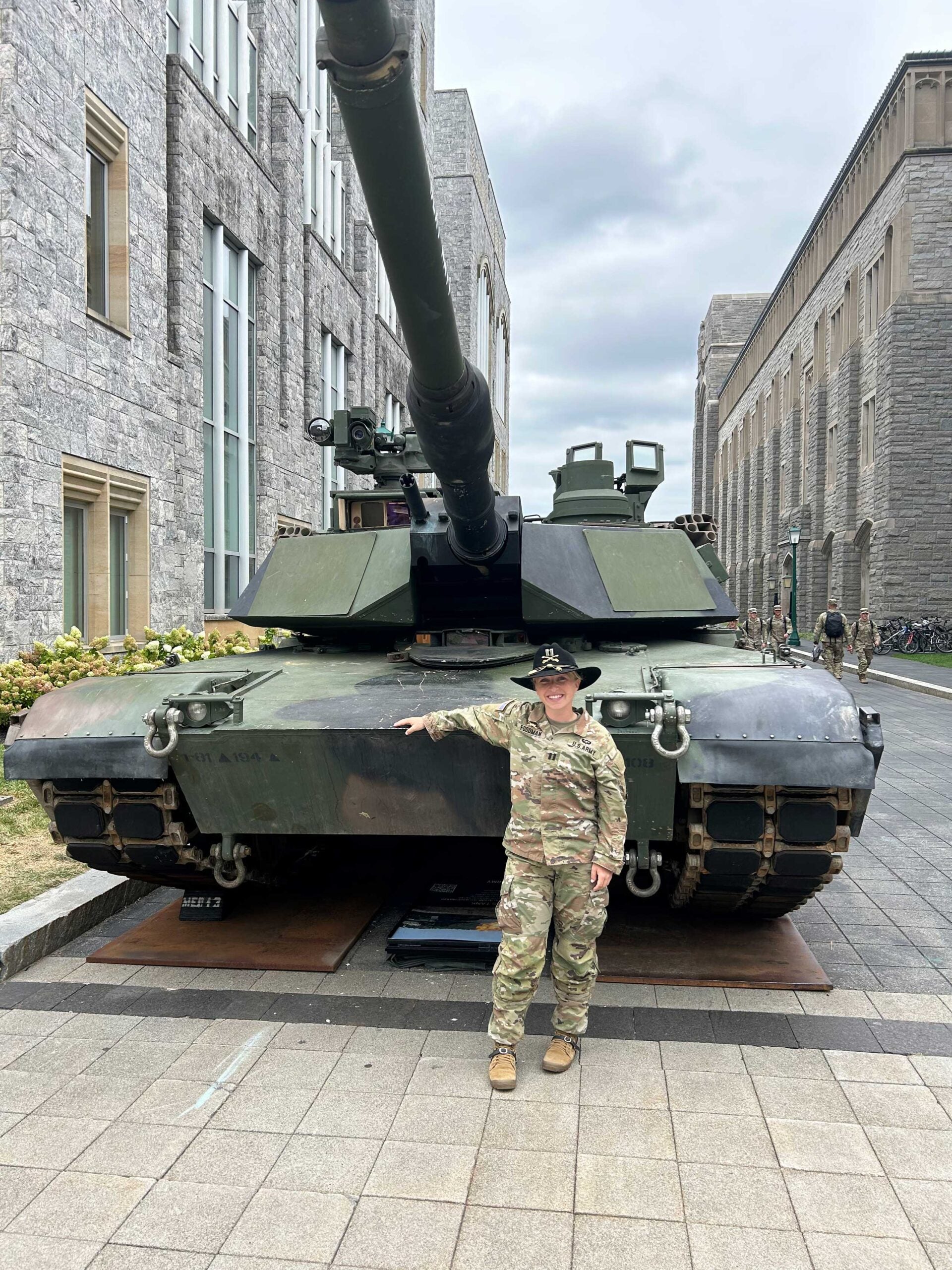 Woman in military uniform standing in front of a military tank displayed on campus.