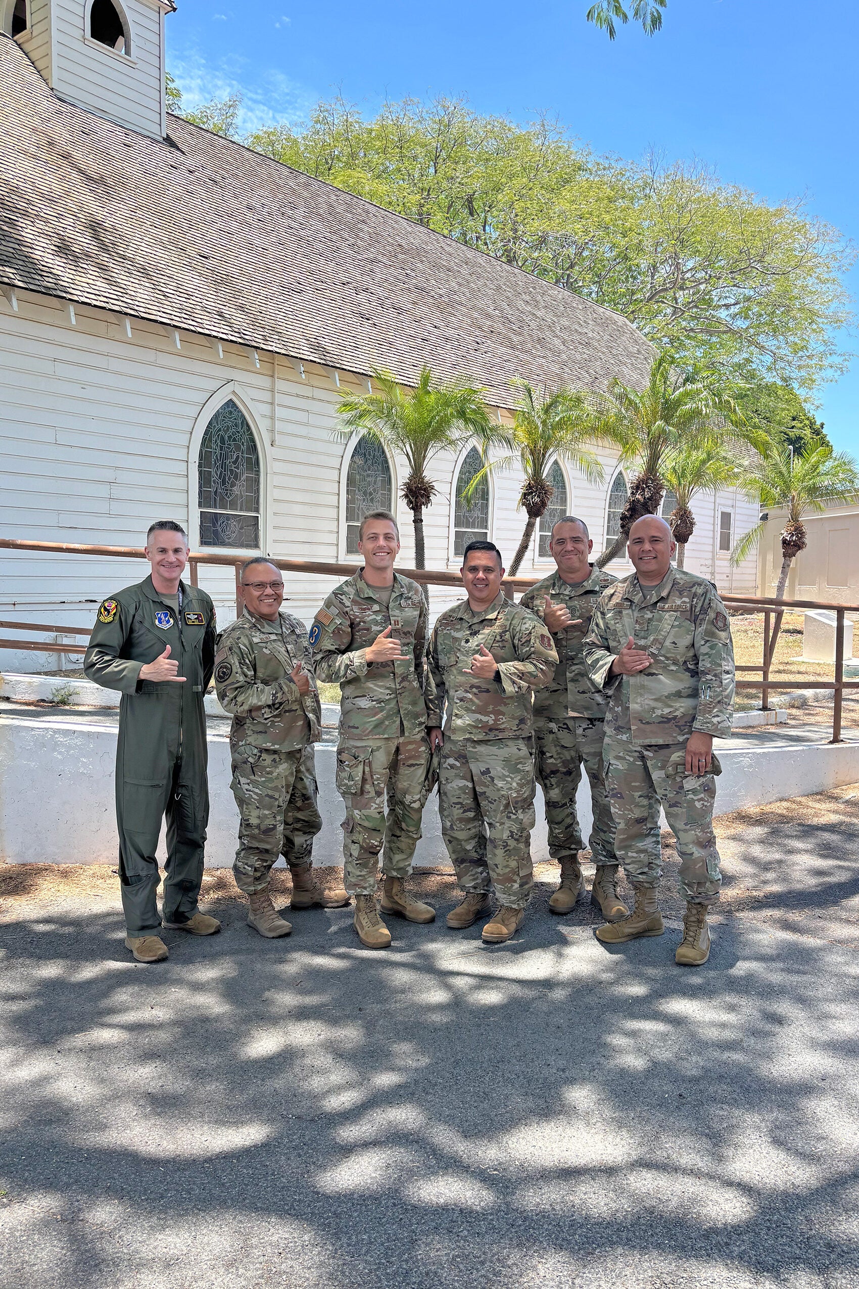 Six men in in military uniform pose for a group photo near a building.