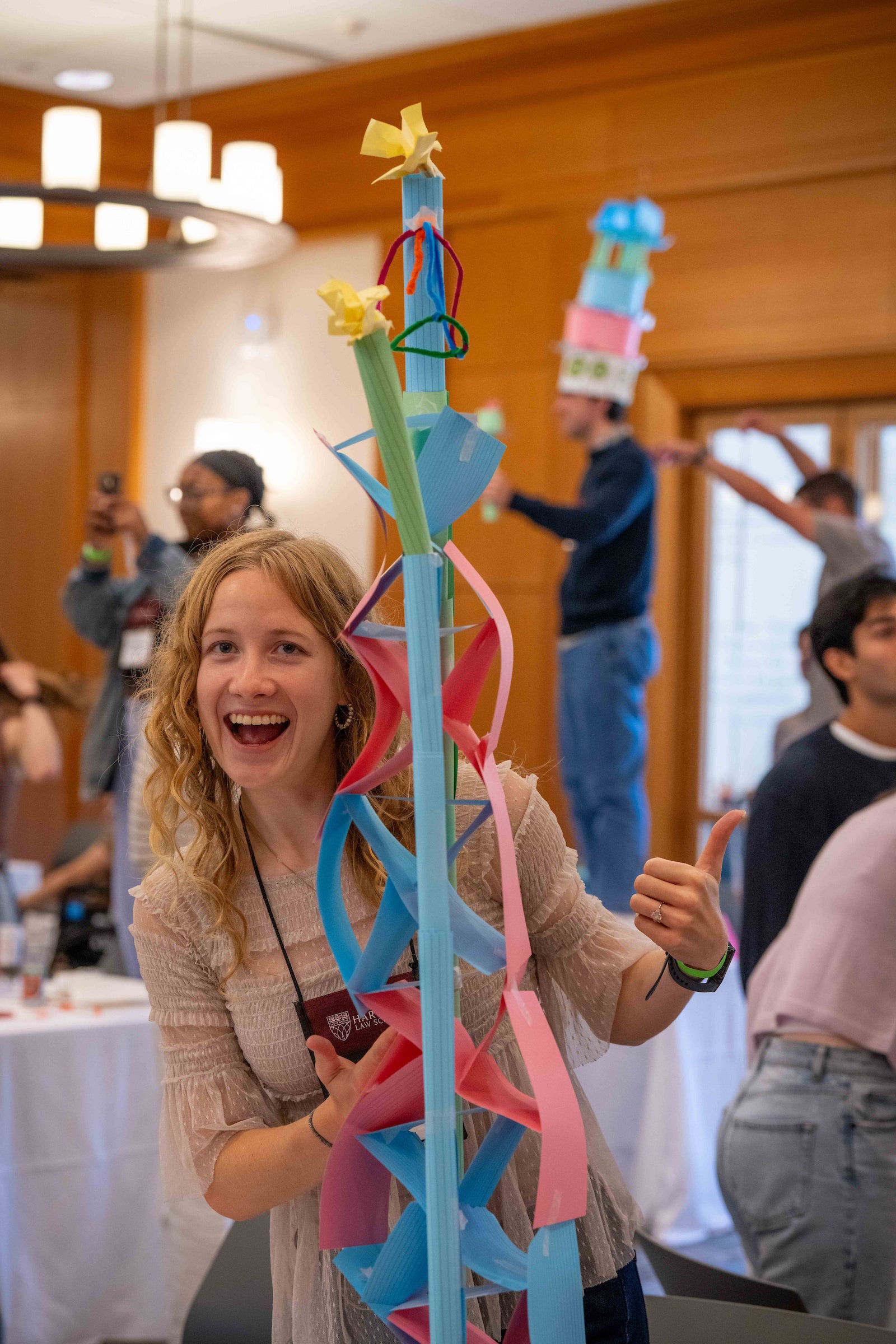 A woman stands in front of a paper structure that she built.